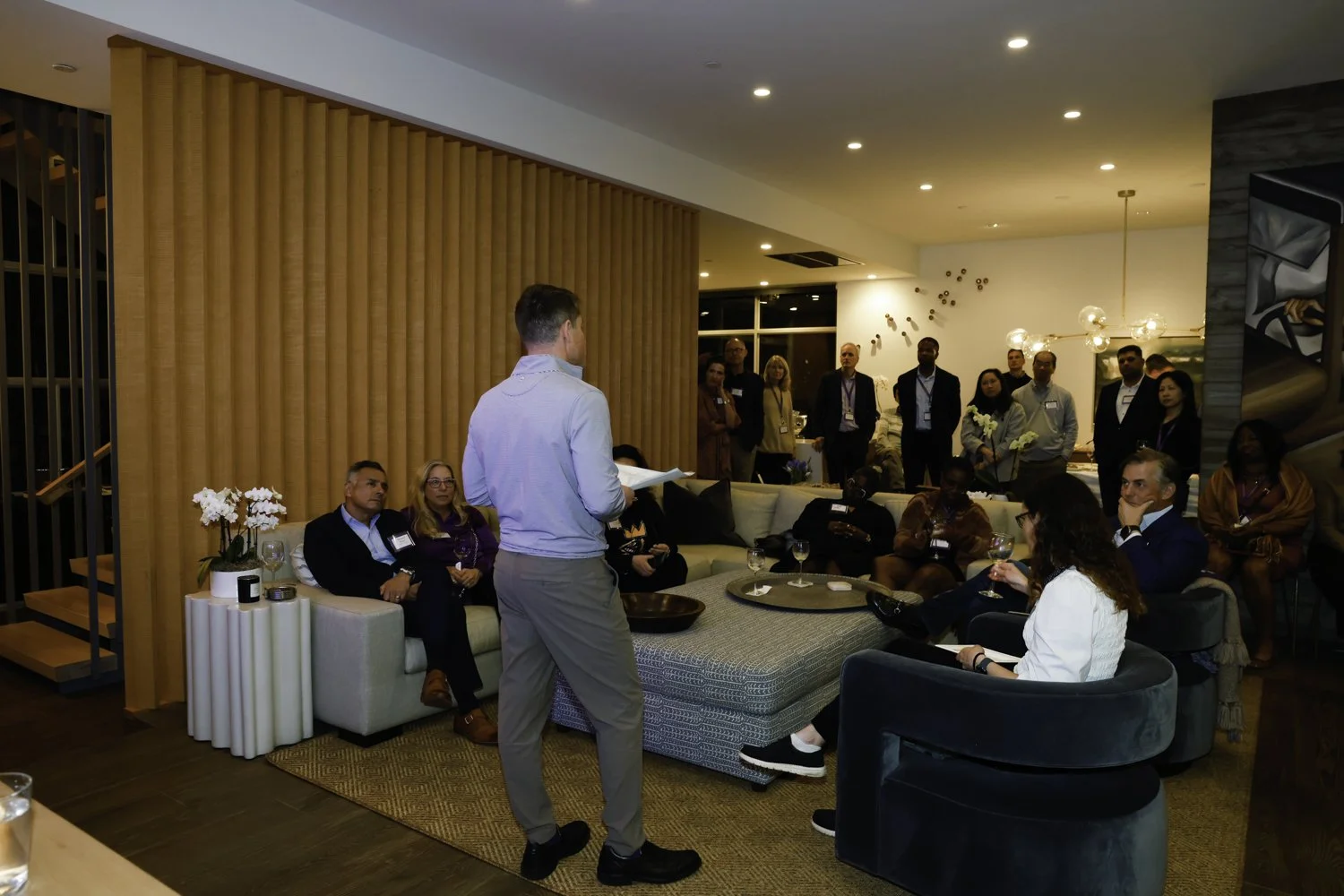 Man giving presentation to a group of diverse professionals seated on sofas and chairs in a modern, well-lit room with decorative art and flowers at Northwestern fundraiser in San Francisco, CA.