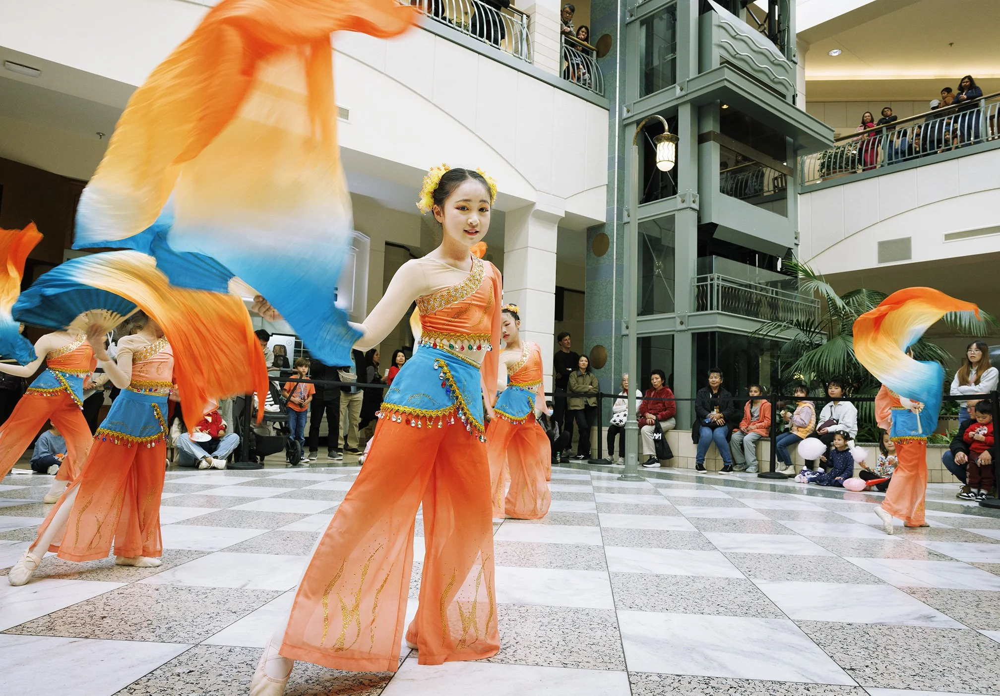 Group of young Asian girls in costumes with one girls standing in front waiving with a silk scarf in her hand performing a dance in a shopping mall for the Lunar year celebrations in San Francisco, CA.
