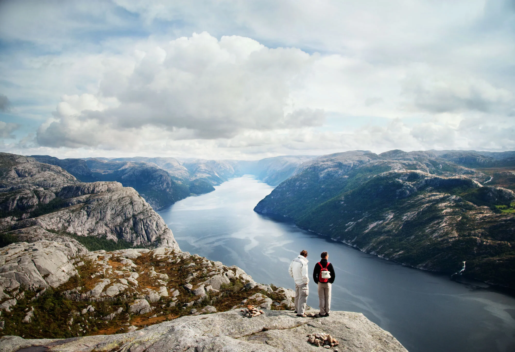 Two young men standing overlooking a fjord and majestic views against a cloudy sky near the Pulpit Chair in Norway.