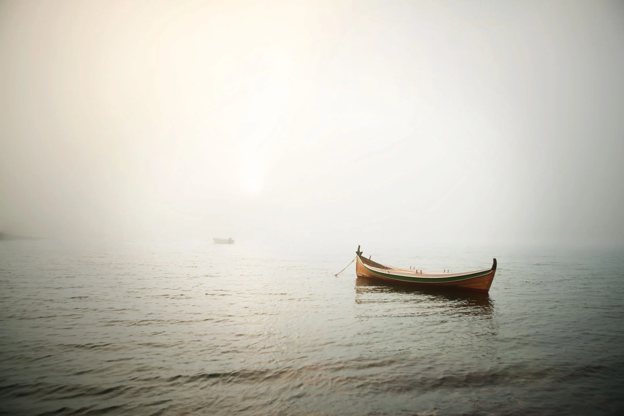 A monochromatic view of a wooden rowing boat out on the water enveloped in fog and some light coming through in Lofoten, Norway.