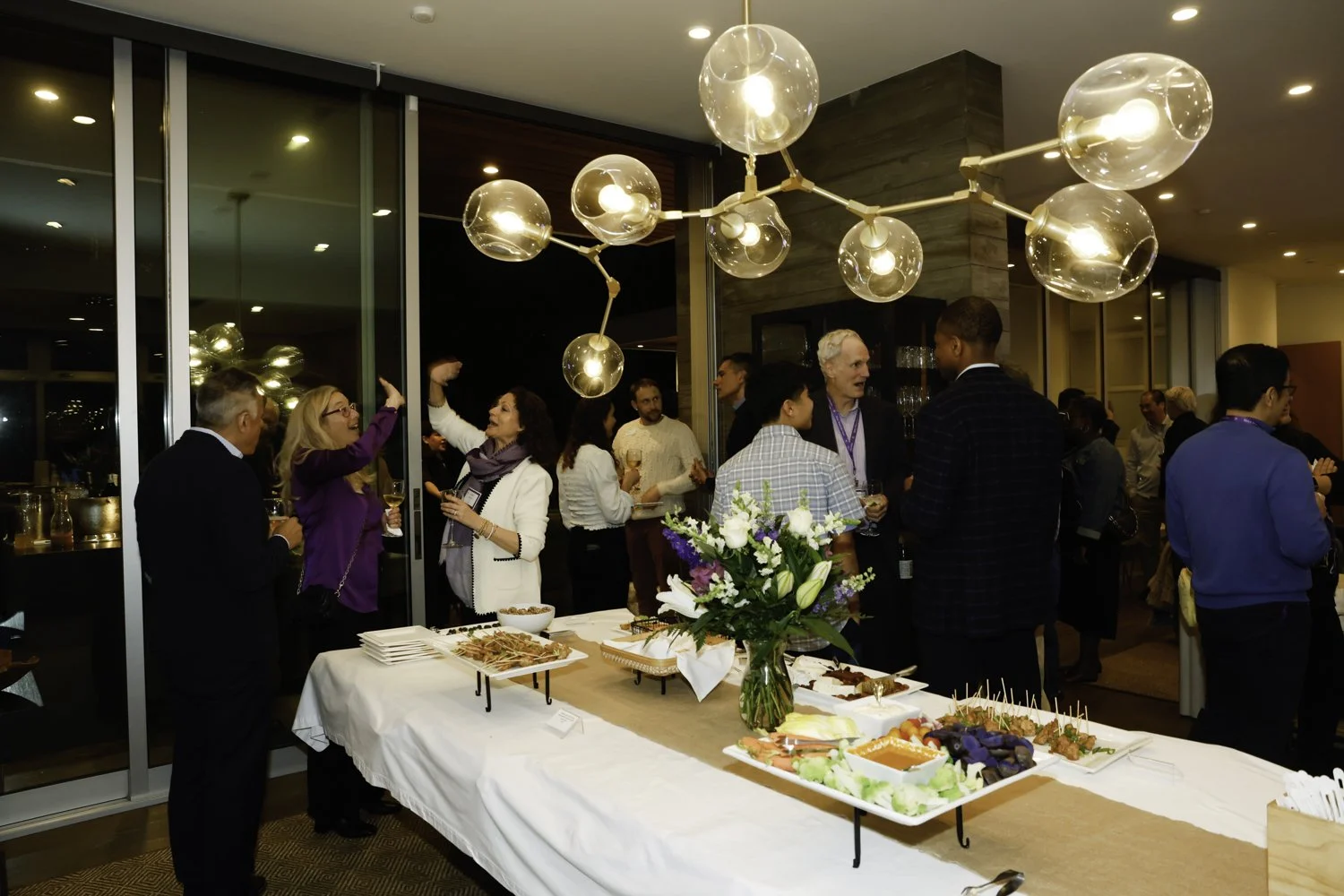 People socializing at a cocktail party in a modern event space with a buffet table and contemporary lighting fixtures at Northwestern fundraiser in San Francisco, CA.