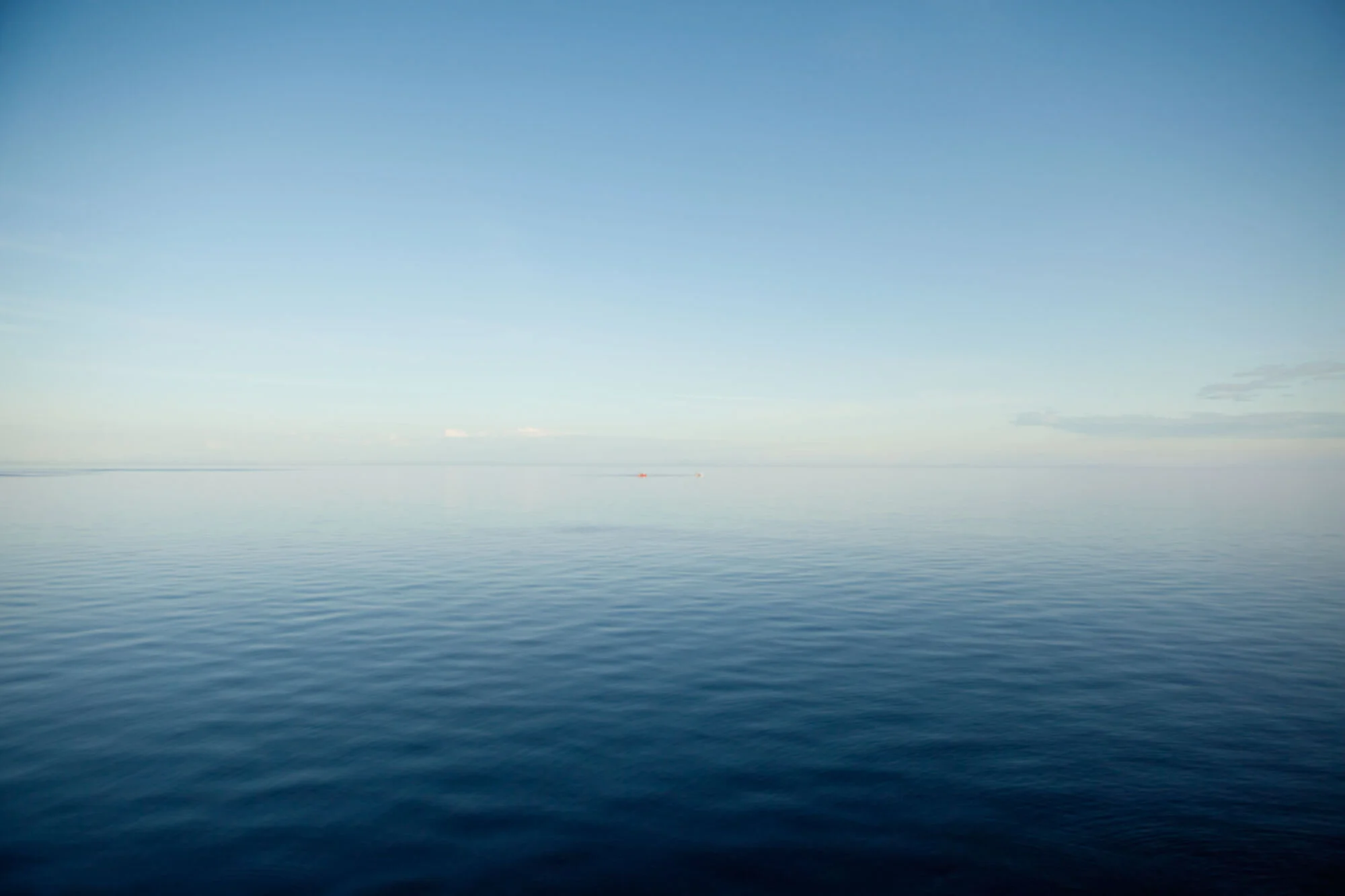 Infinity water and sky that meet midway with a small red dot of a boat in Lofoten, Norway.