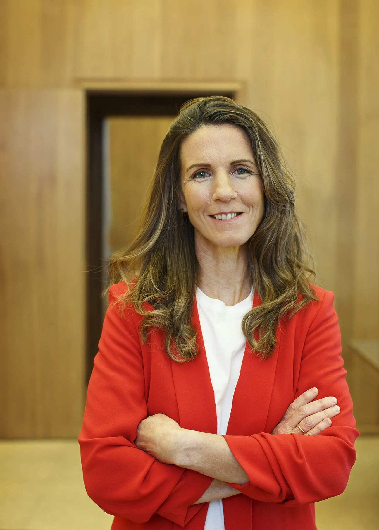 CMO of Hewlett Packard standing in teh infamous wooded panel room of Hewlett and Packard, wearing a red blazer and a white shirt, with her hands crossed in front, she has long hair and stands against a wooden paneled wall in Palo Alto, CA.
