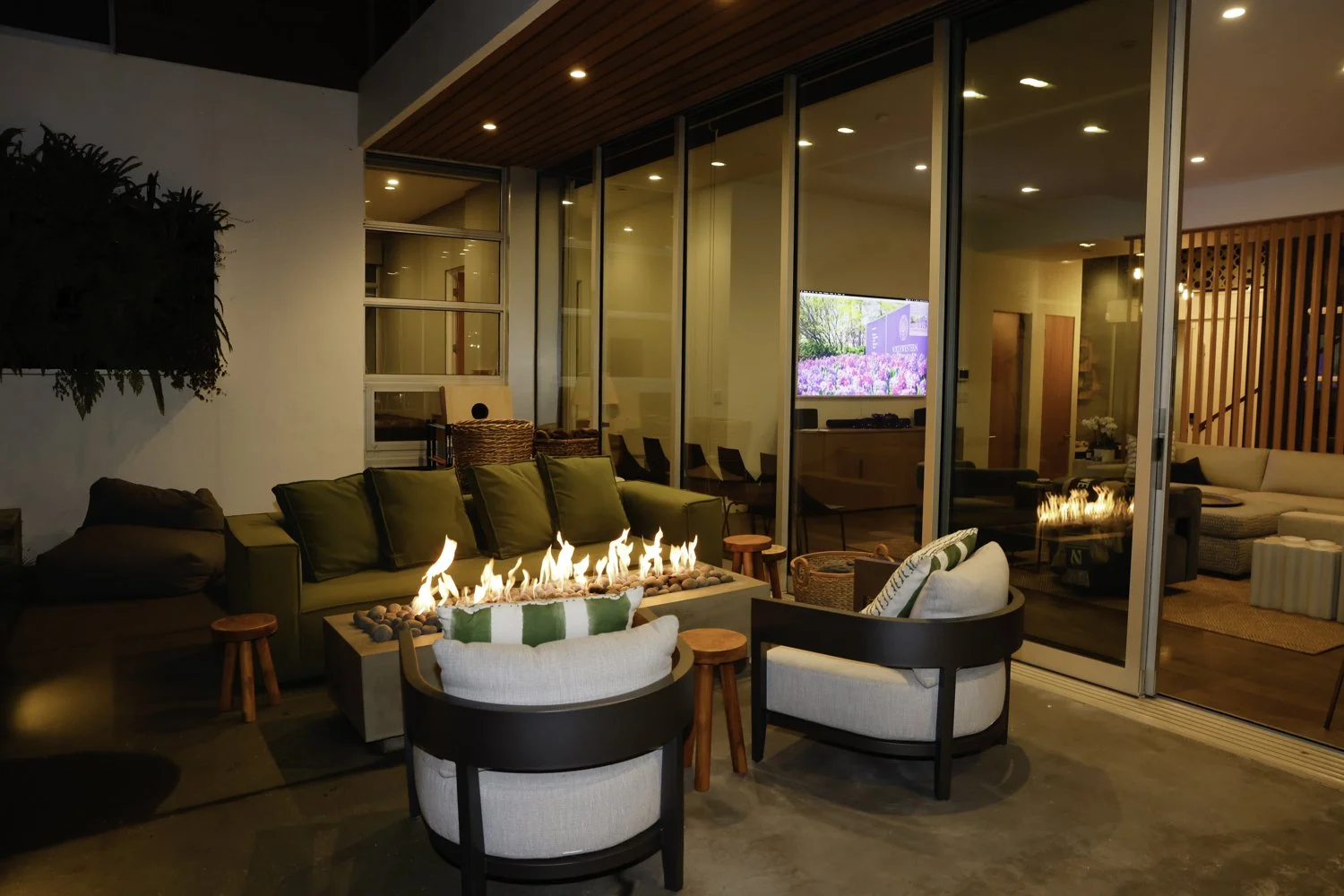 Indoor and outdoor living space featuring a fire pit with flames, seating with cushions, and a view into a room with a television and additional furniture Brex headquarter in San Francisco, CA.