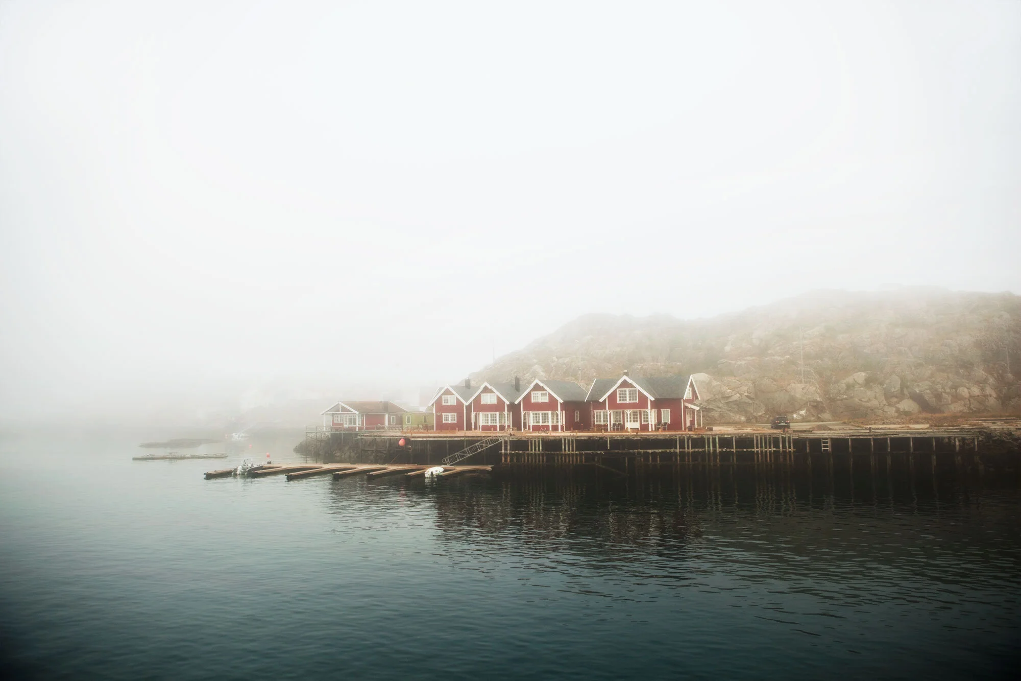 Red, wooden fishing huts on an island in Lofoten, Norway with dense fog covering the hillside.