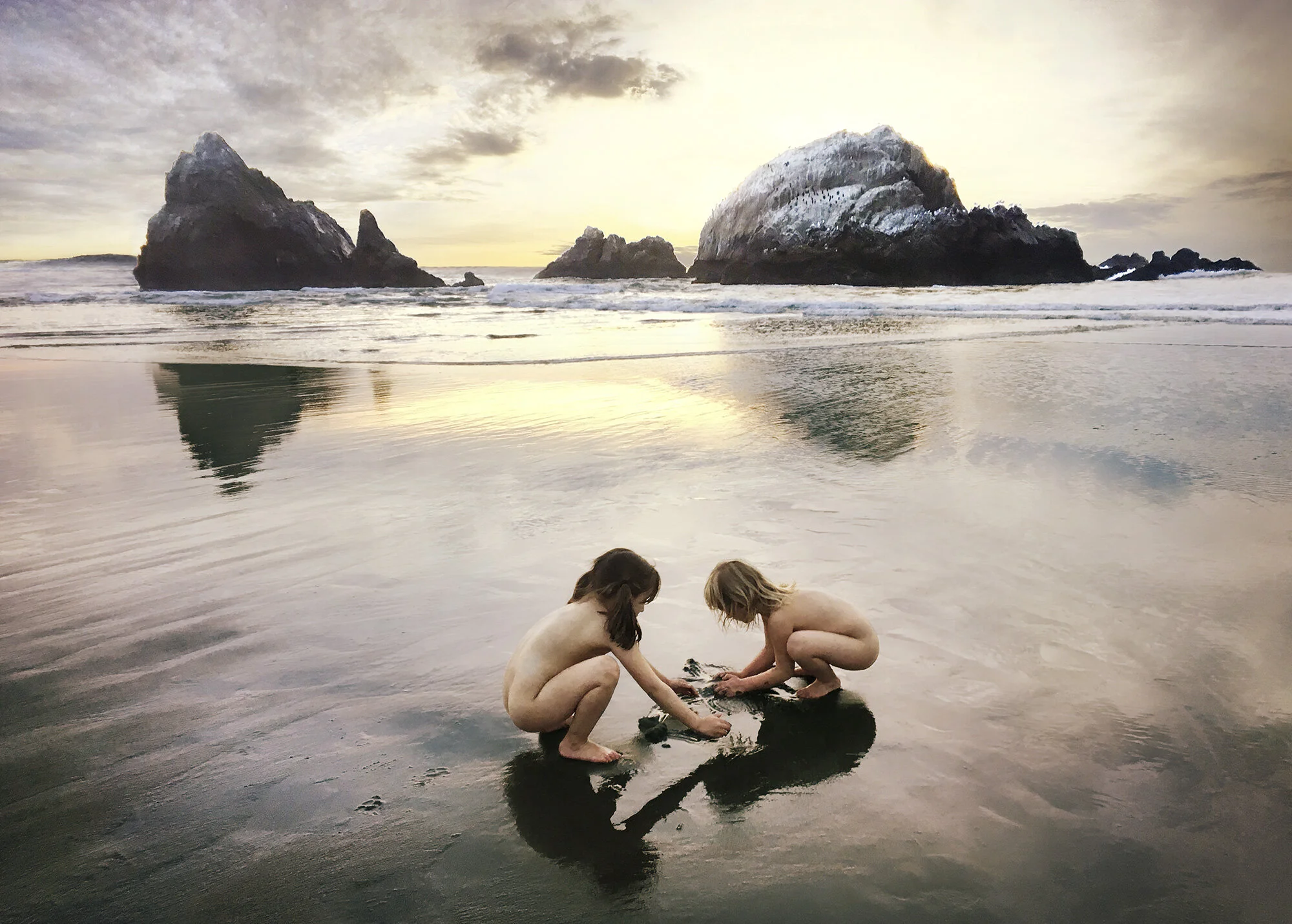 Two very young girls playing in the sand against some rocks in the background at sunset with purple and yellow light at Land's End in San Francisco, CA.