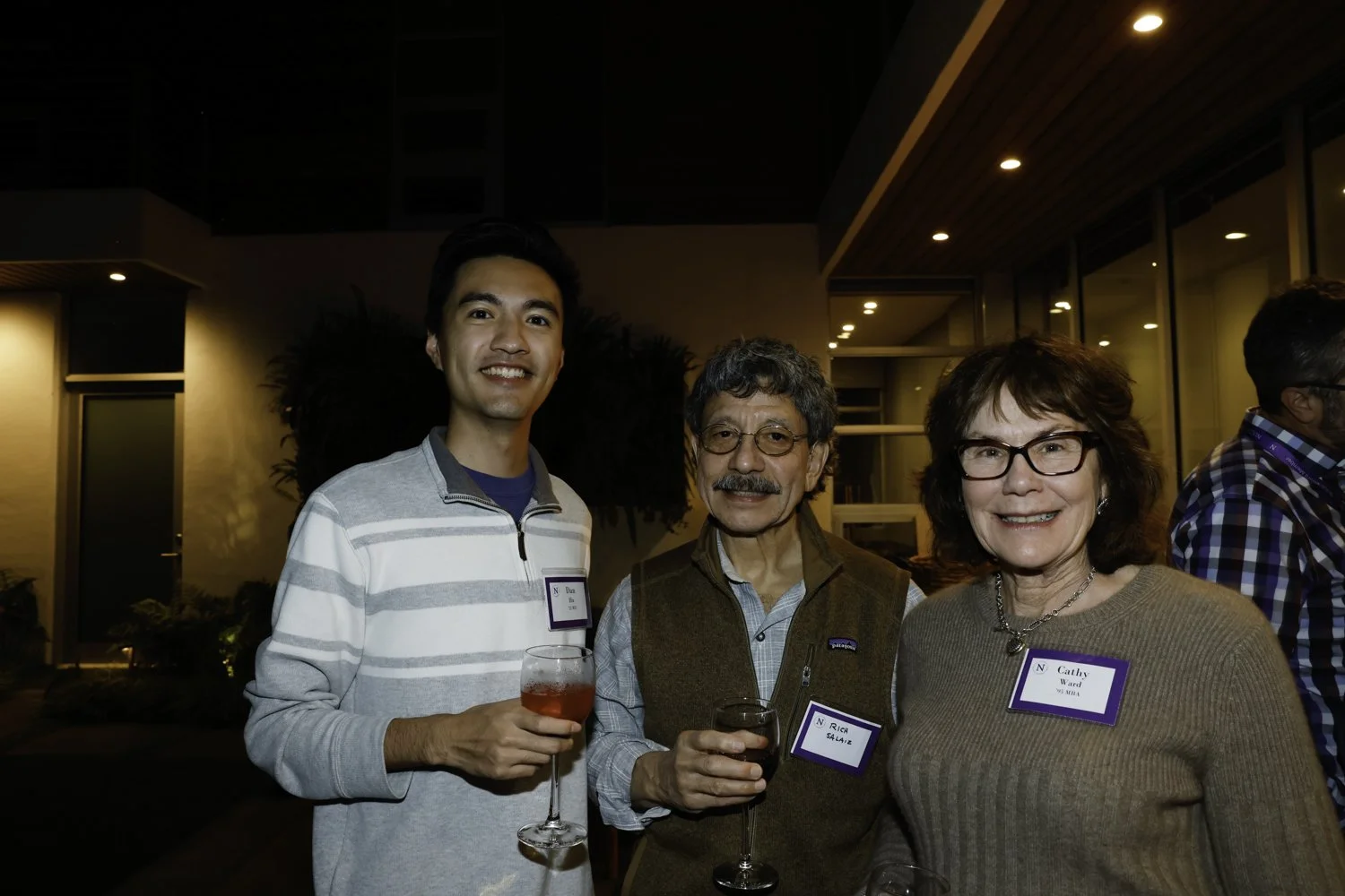 Three people standing together holding drinks at an indoor social event, with name tags visible on their clothing at Northwestern fundraiser in San Francisco, CA.