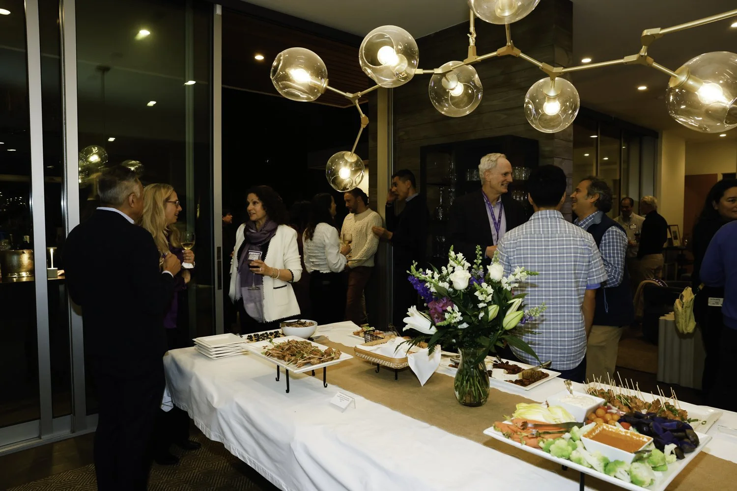 People socializing at a catered event with a table of appetizers and a floral centerpiece at Northwestern fundraiser in San Francisco, CA.