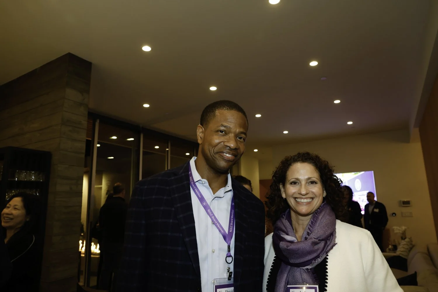 Two smiling professionals, a man and a woman, at a social event in an indoor setting with warm lighting and other attendees in the background at Northwestern fundraiser in San Francisco, CA.