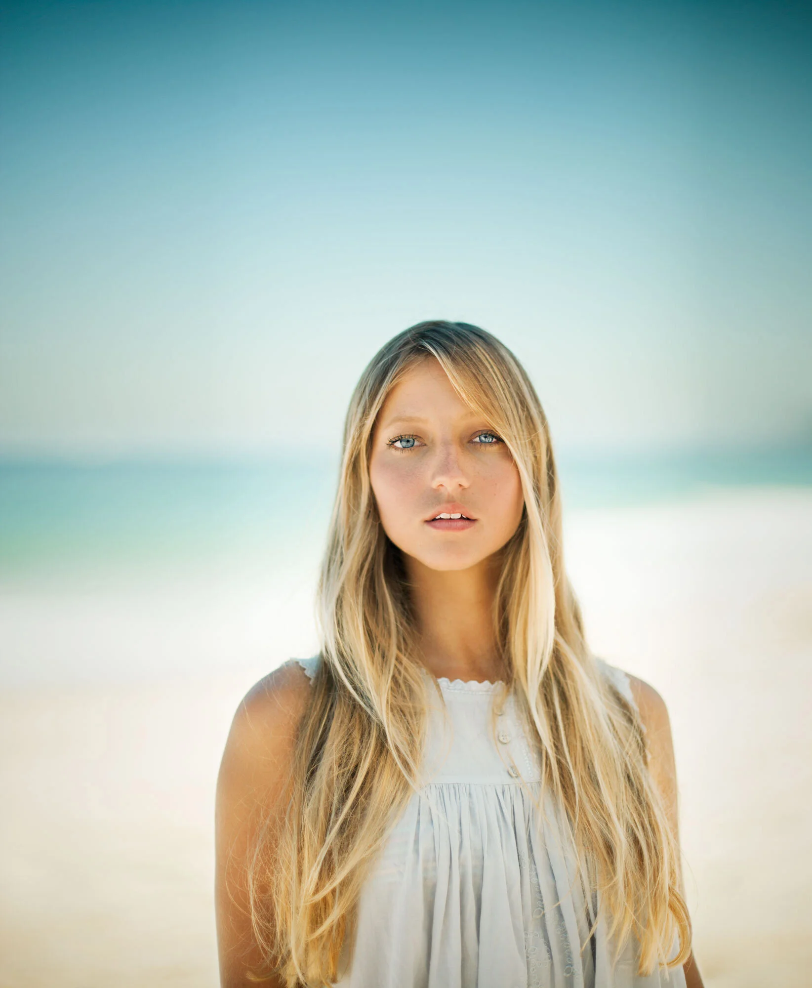 Young Brazilian woman with long blonde hair and blue eyes standing on a beach with sand and ocean in the background in Ipanema Beach, Rio de Janeiro, Brazil.