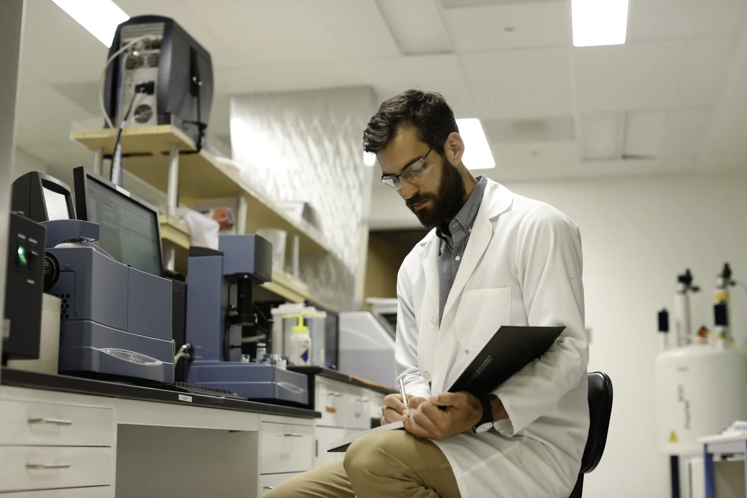 A scientist with glasses is taking notes inside a laboratory with white walls. Science lab in San Francisco, CA.