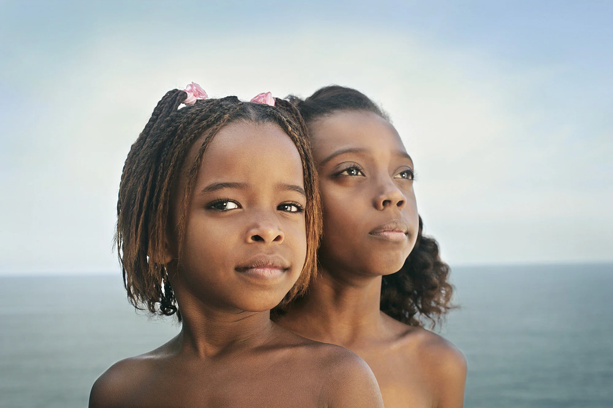 Two young Black girls with long hair standing by the ocean, facing slightly away from the camera looking proud and strong at Ipanema bach in Rio de Janeiro, Brazil.