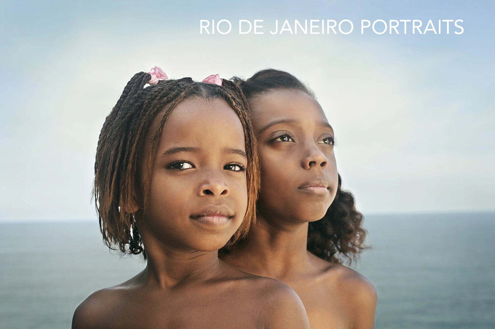 Two young Black girls with expressions of confidence looking at the camera, with an ocean in the background, against the Atlantic ocean in Rio de Janeiro, Brazil.