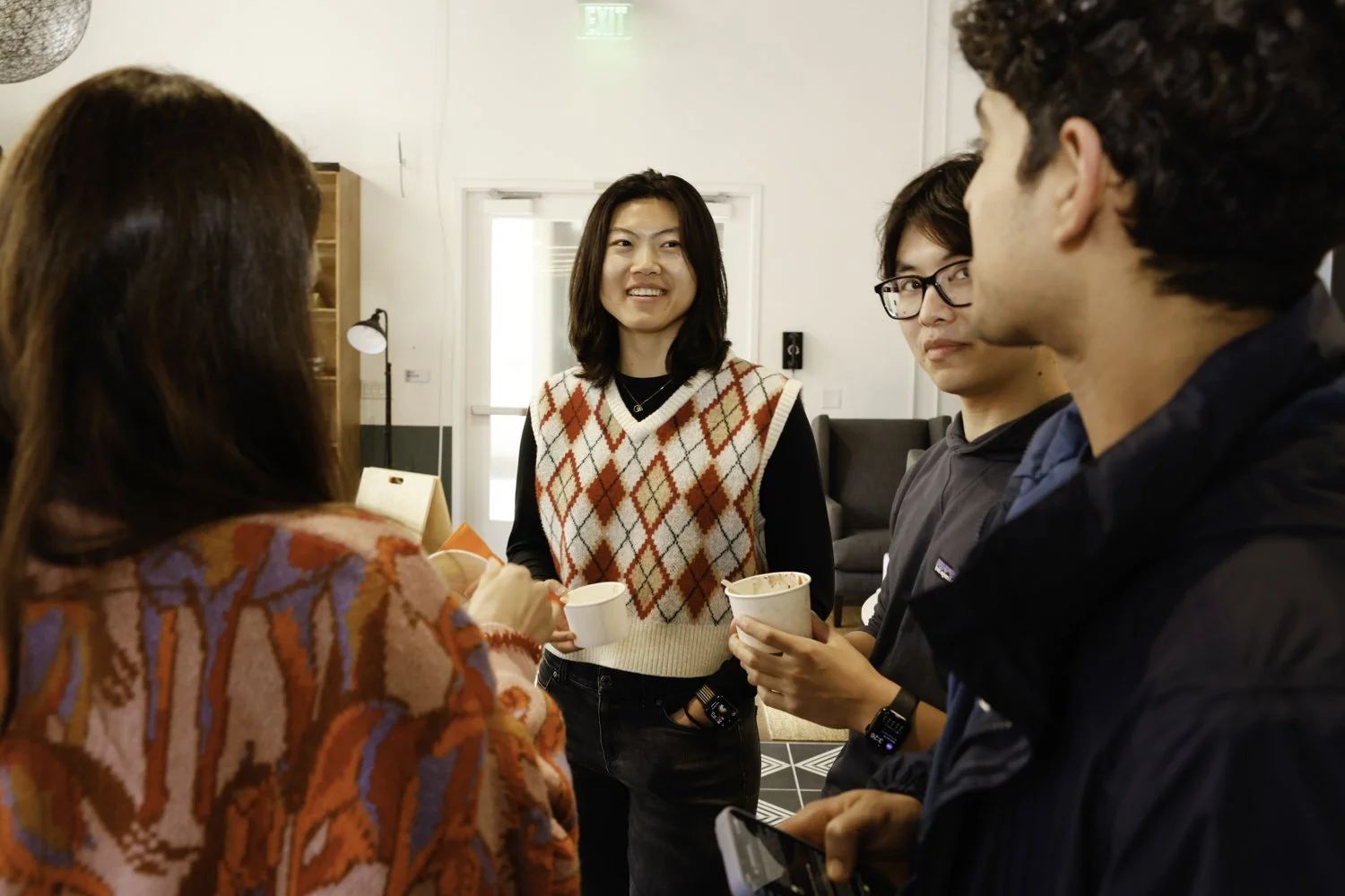 Group of five young adults having a casual conversation indoors, some holding cups and a phone Brex headquarter in San Francisco, CA.
