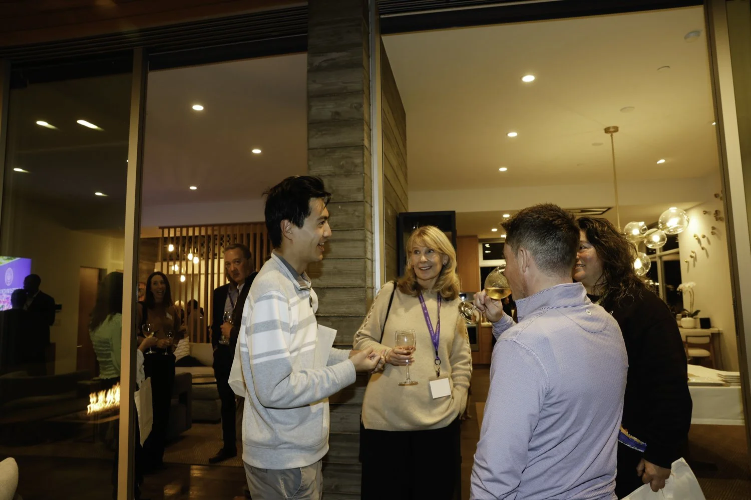 Group of people talking and socializing at a party or gathering in a warmly lit indoor space, with some holding wine glasses at Northwestern fundraiser in San Francisco, CA.