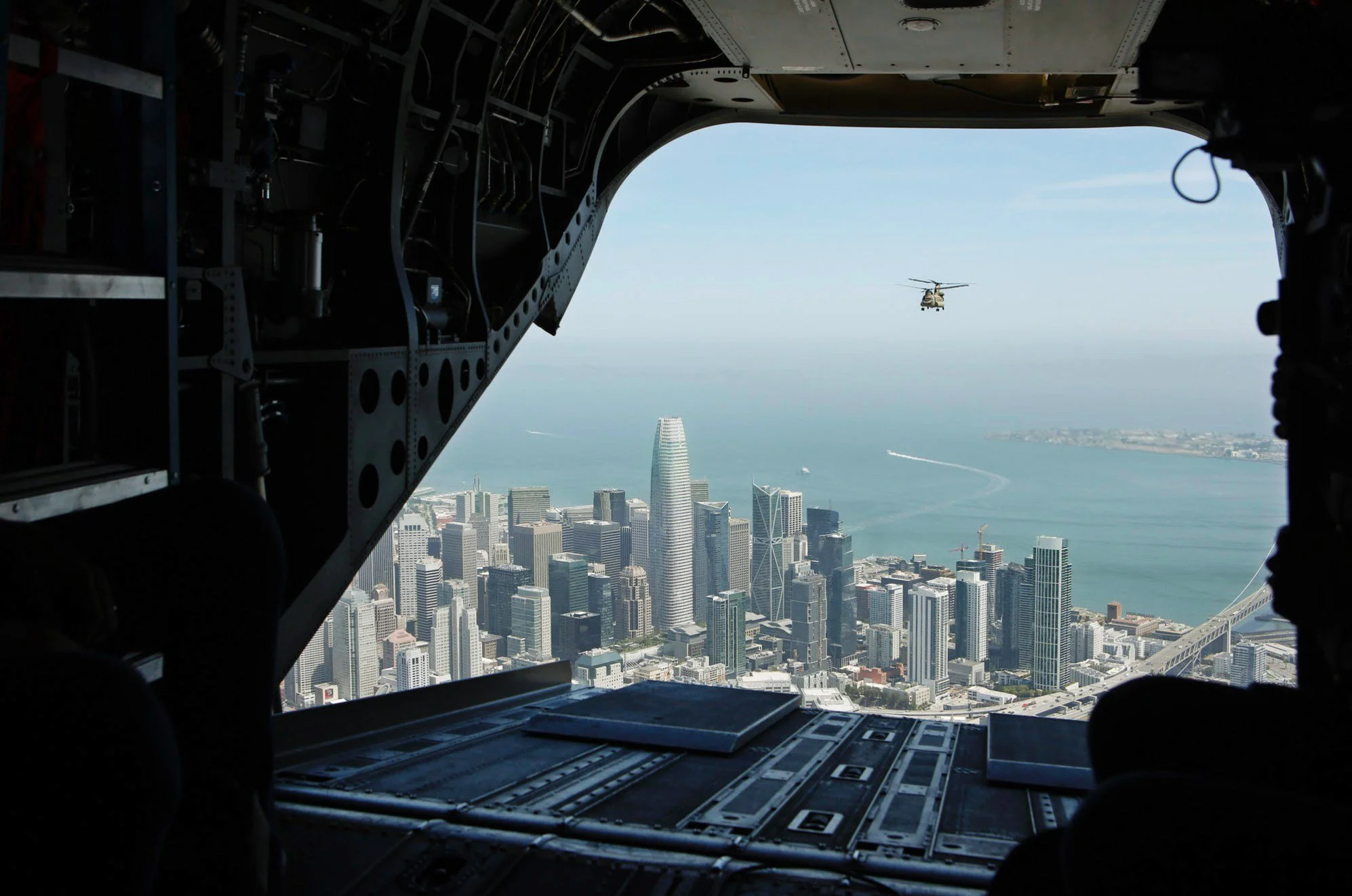 Inside a darkly lit military helicopter with the backdoor open where you see another helicopter flying behind over San Francisco in the distance photographed for Salesforce Trailhead Military (Military Veteran Recruitment Strategy) on location in Cal