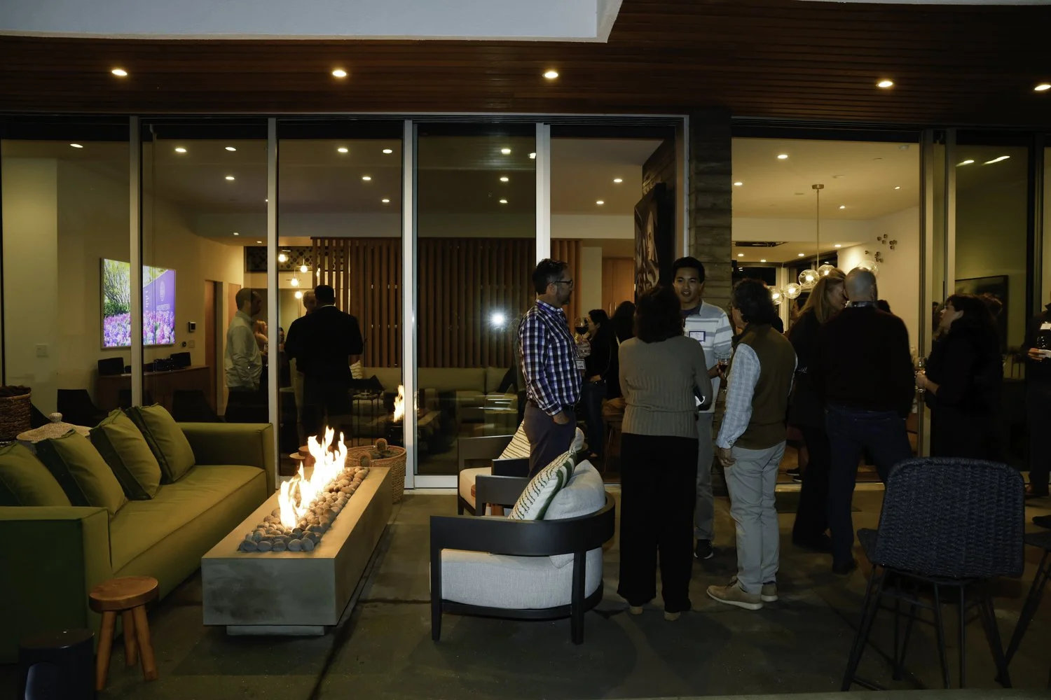 Group of people socializing at an indoor-outdoor party with a fireplace, modern furniture, and large glass doors at Northwestern fundraiser in San Francisco, CA..