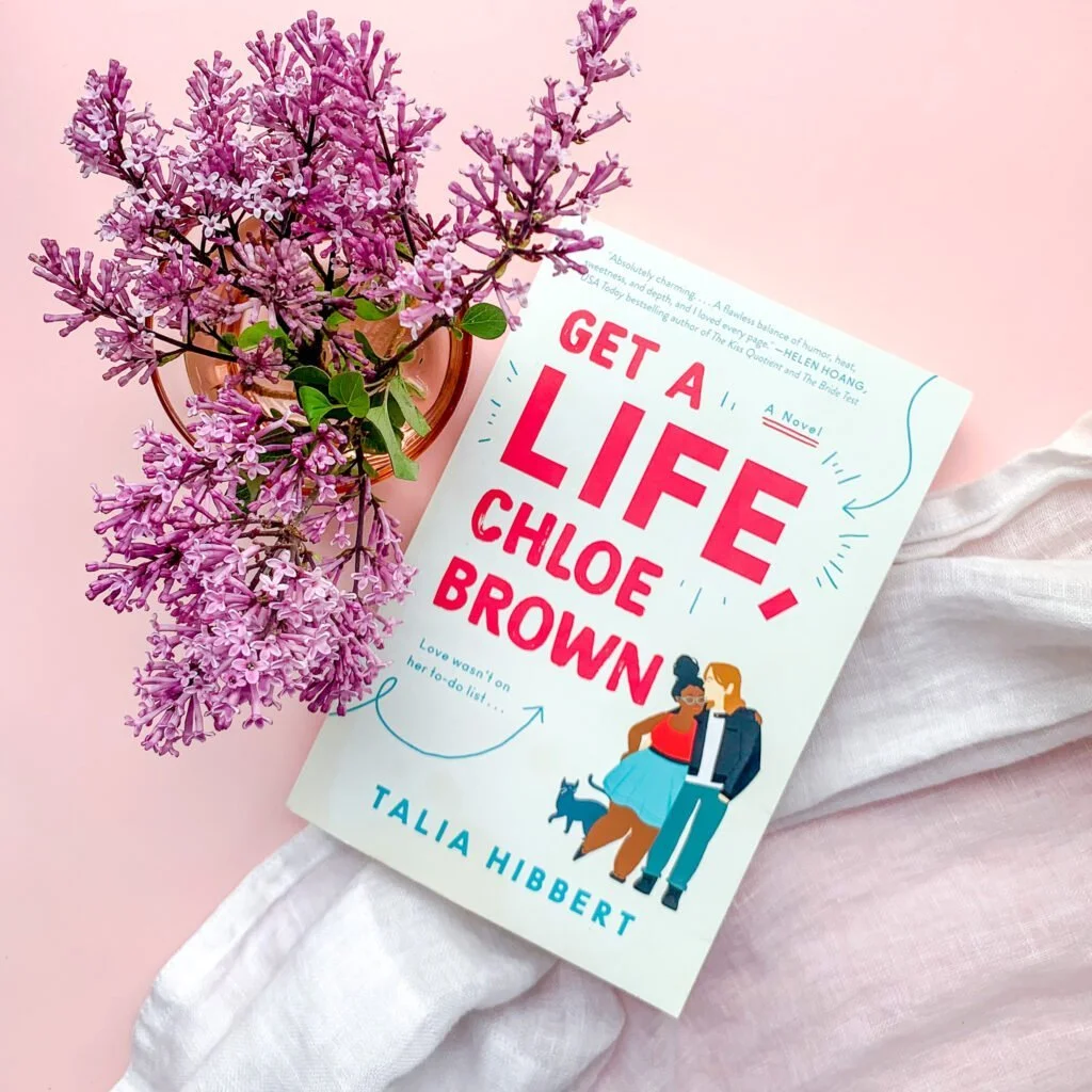 Photo of book on a table with bouquet of lilacs.