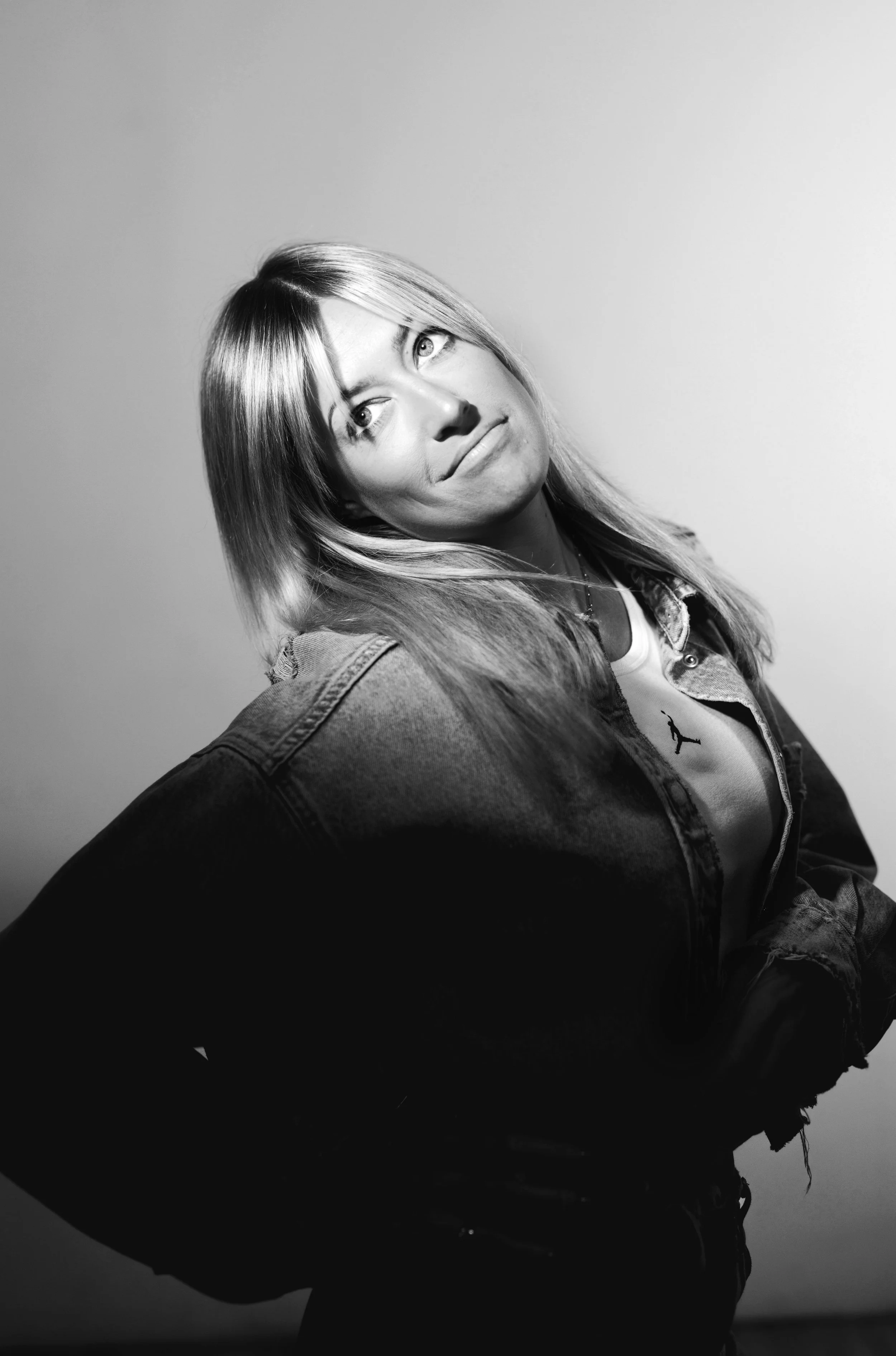 Black and white portrait of a young woman with shoulder-length hair, wearing a denim jacket and a white top, looking slightly upward with a thoughtful expression.