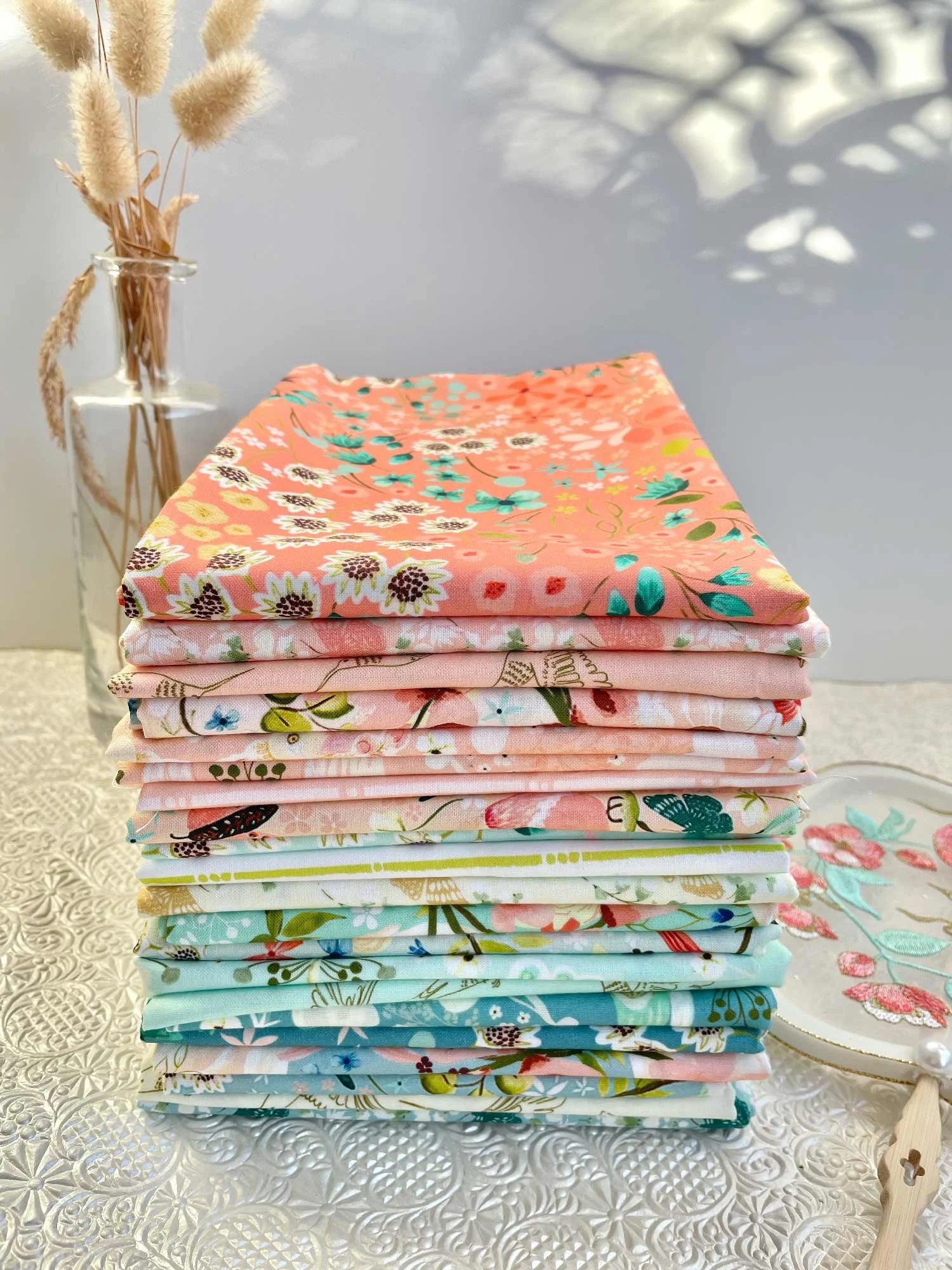 Stack of Serenity Blooms fabric by Ginger Deverell with colours ranging from coral to mint green, peach and blue