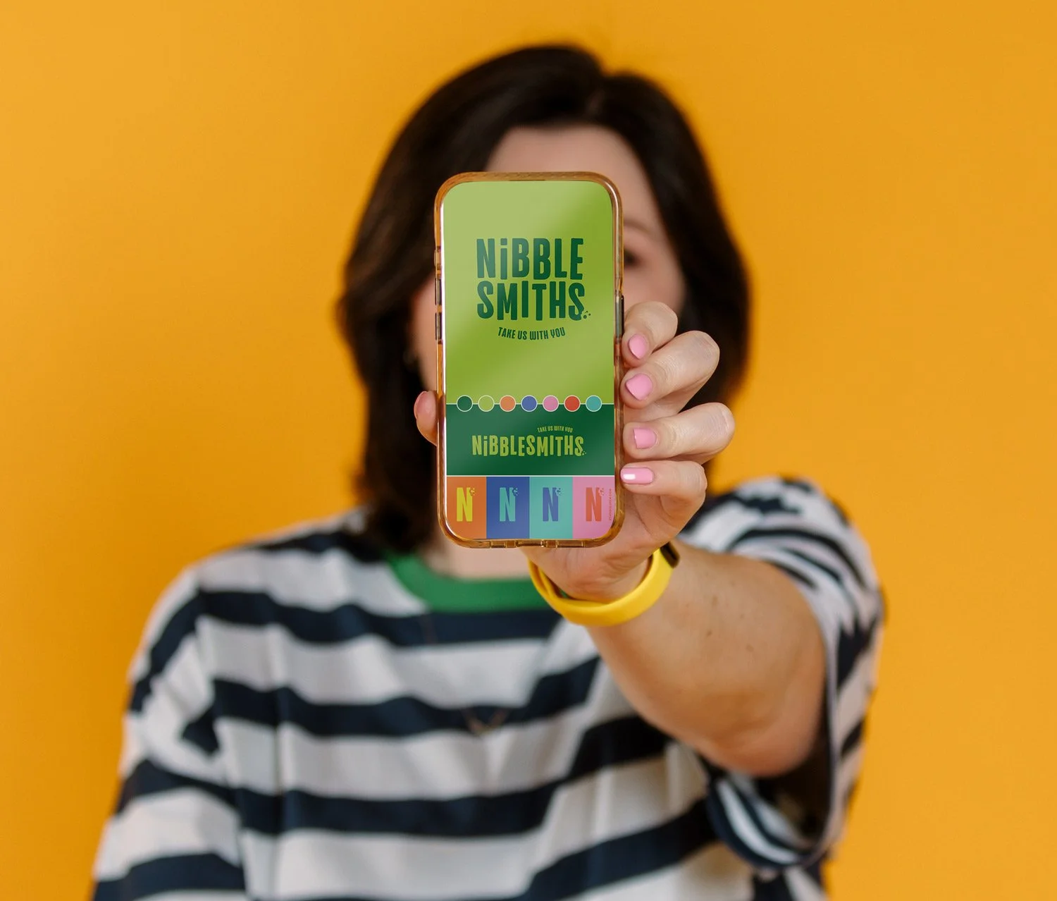 Photo of Amy against a yellow backdrop holding a phone up to the viewer
