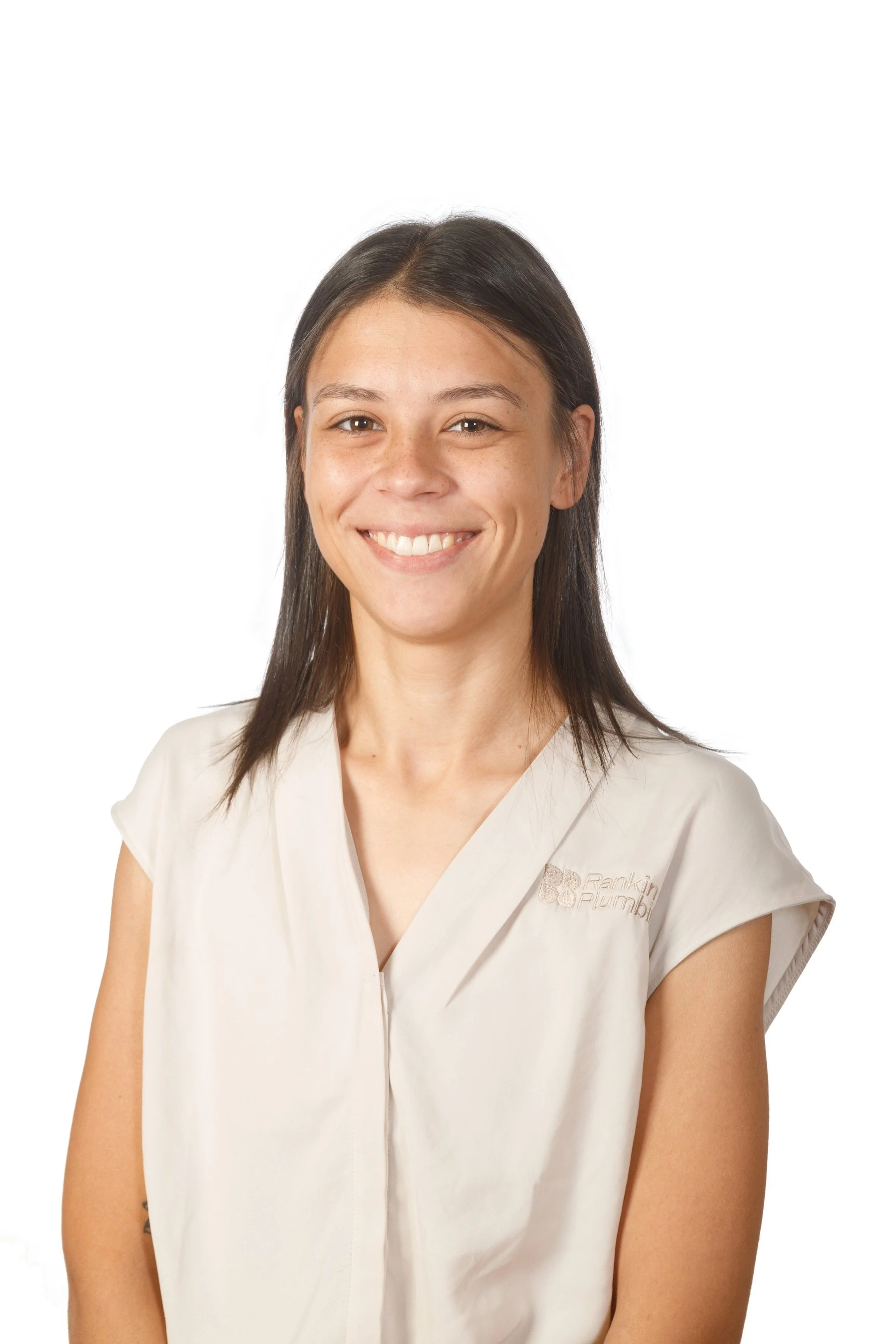 A woman with brown hair smiling, wearing a beige shirt with embroidery, against a plain white background.