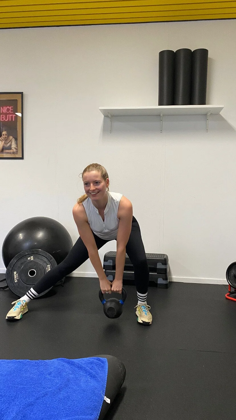 Vrouw doet een fitnessoefening met een kettlebell in een sportschool.