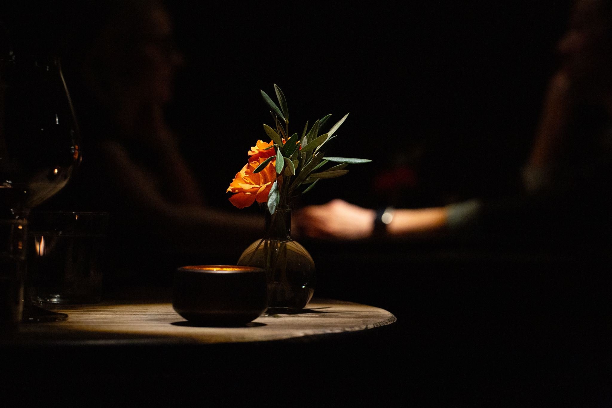A small vase of orange roses and a candle on a table