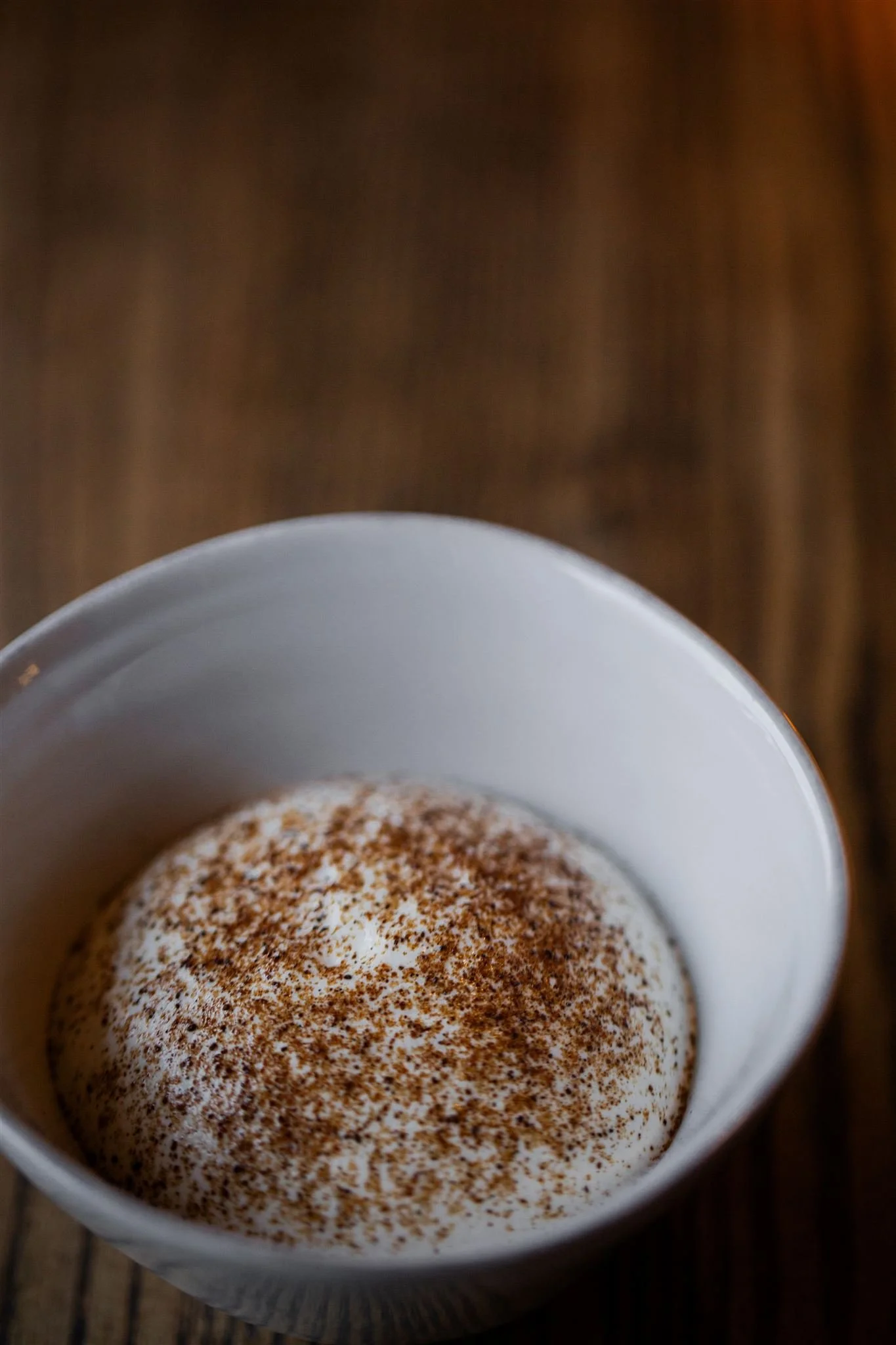 A white bowl of a creamy dessert dusted with spice