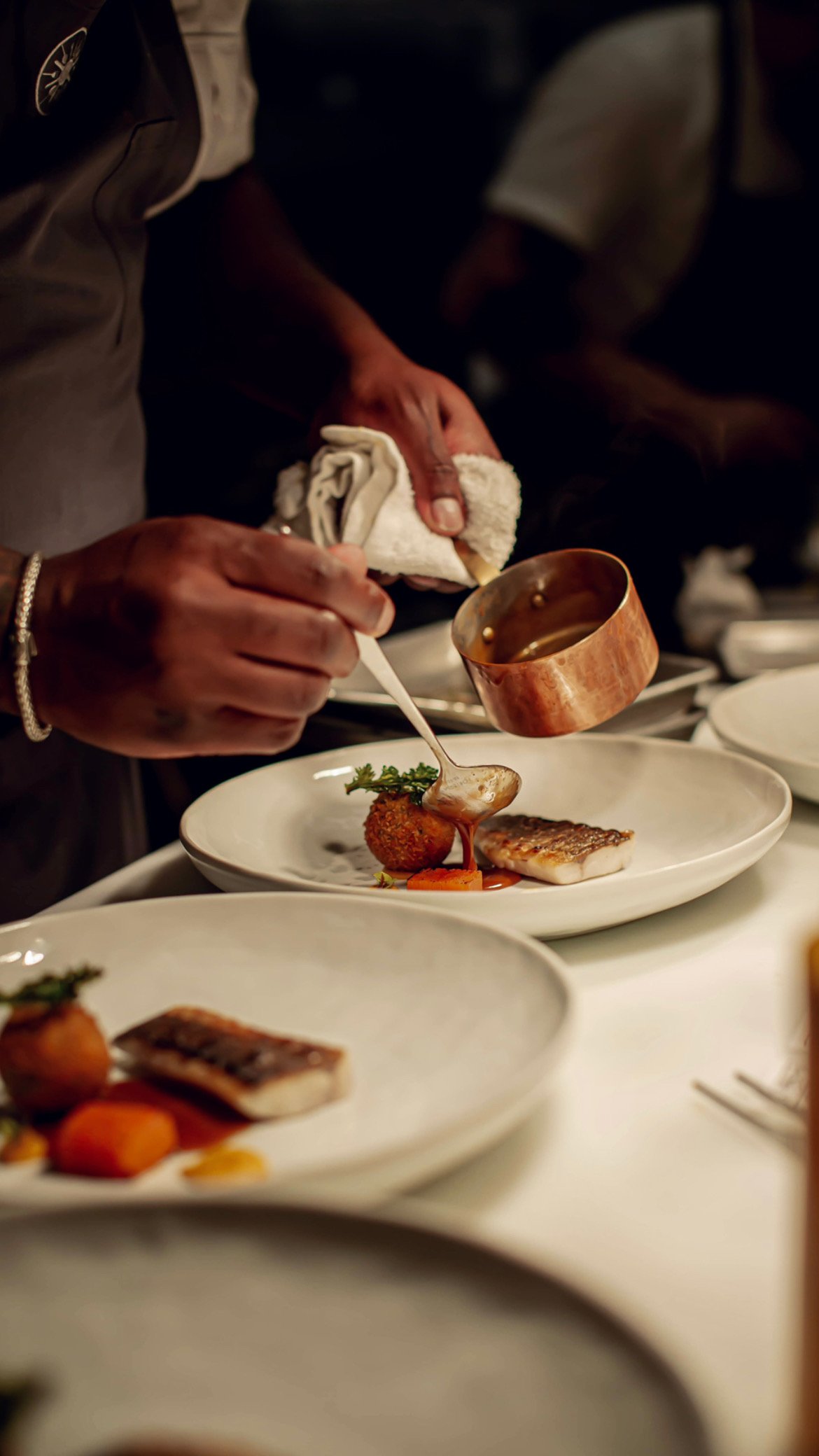 A cook plating fish and pouring sauce at Table Culture Provisions
