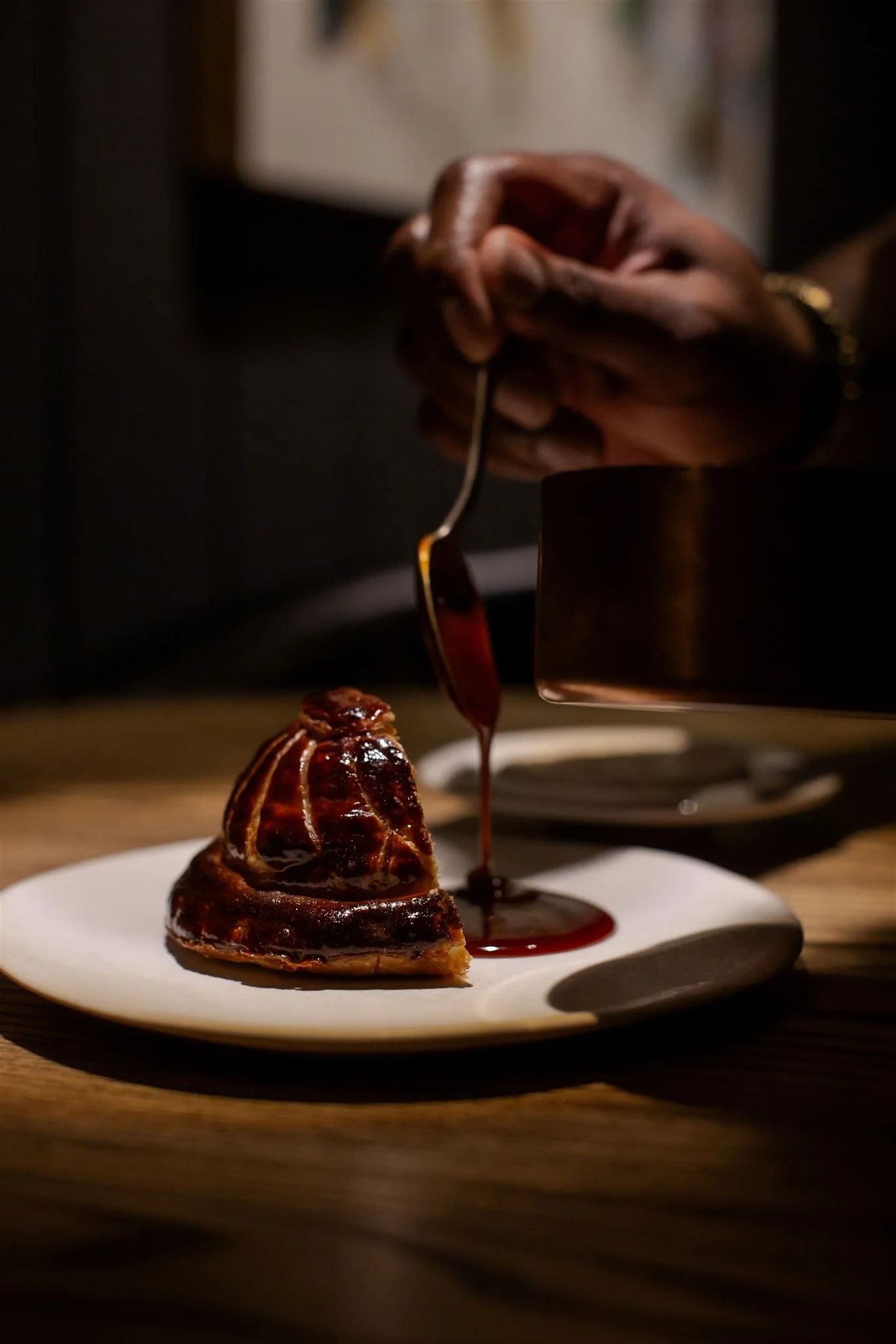 A glazed pastry on a plate while sauce is poured over it