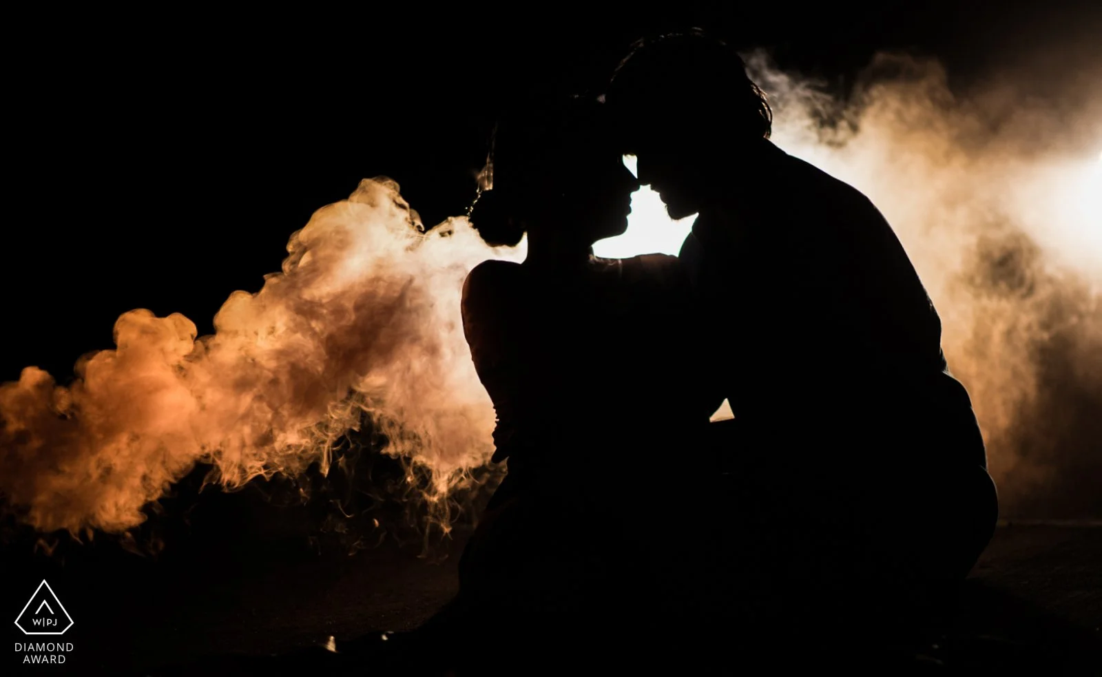 Silhouette of a couple in an intimate embrace at night, with smoke or vapor surrounding them, backlit for dramatic effect.