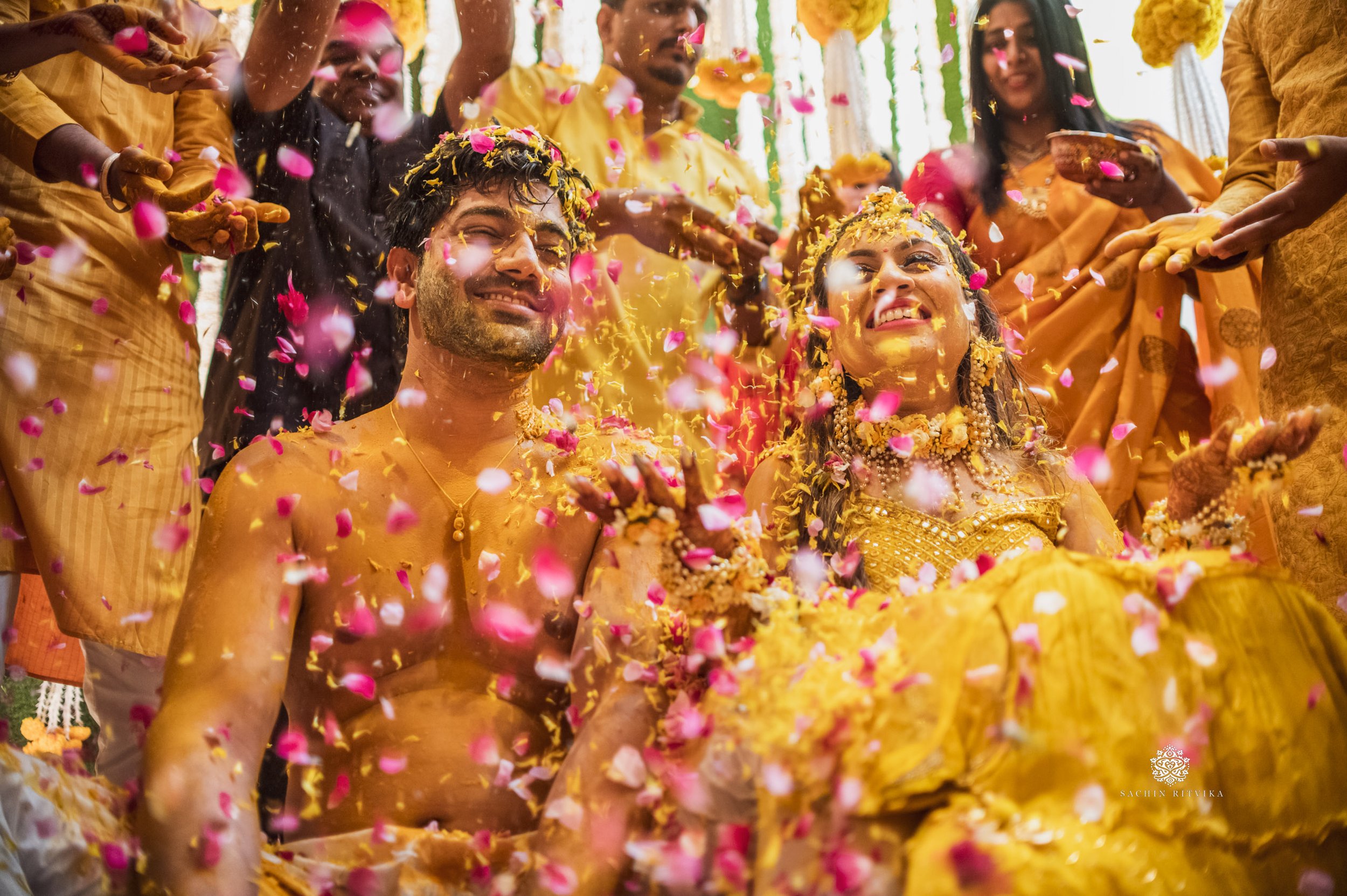 Traditional Indian pre-wedding ceremony with couple covered in turmeric paste and flower petals.