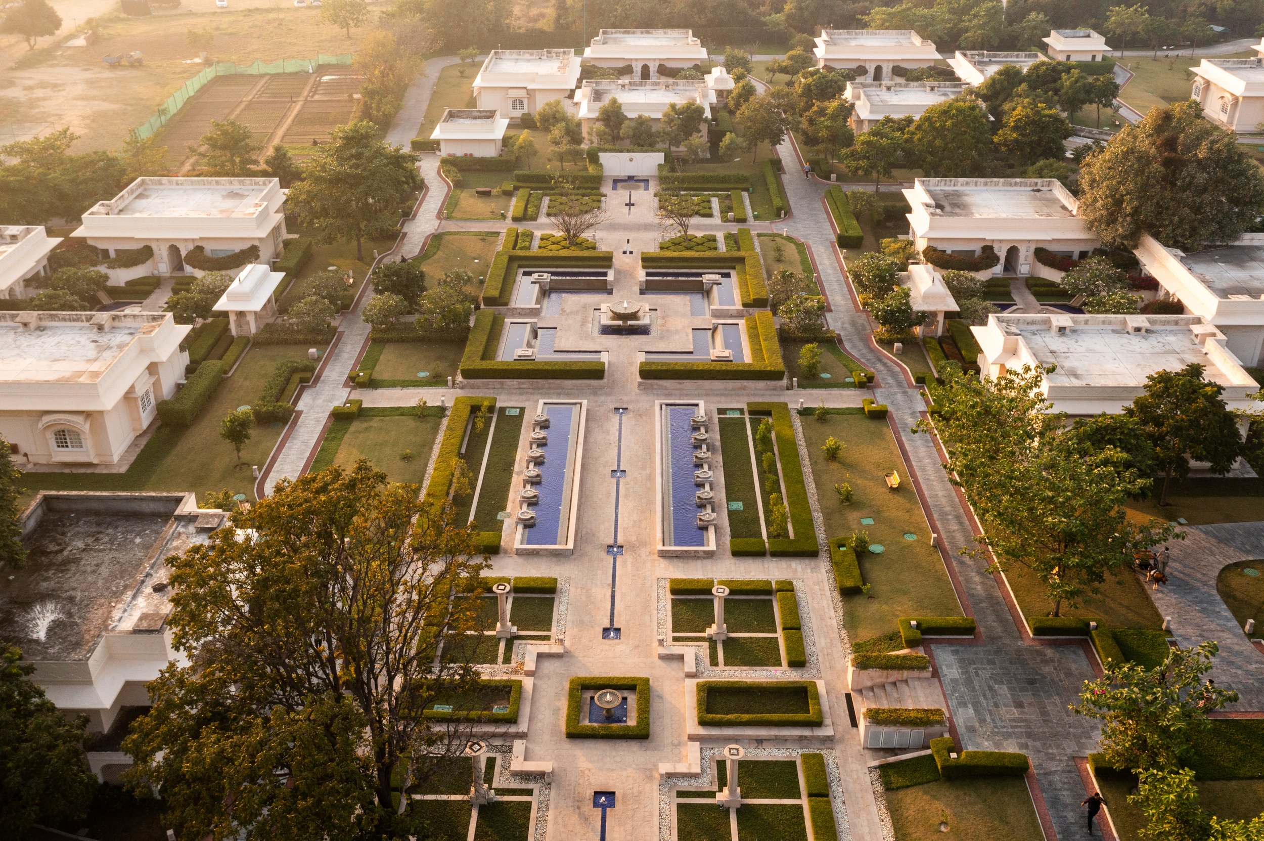 Aerial view of a landscaped garden with pathways and symmetrical layout, surrounded by white buildings and greenery. 7 star property of Sukhvillas, Oberoi Hotels & Resorts, Chandigarh.