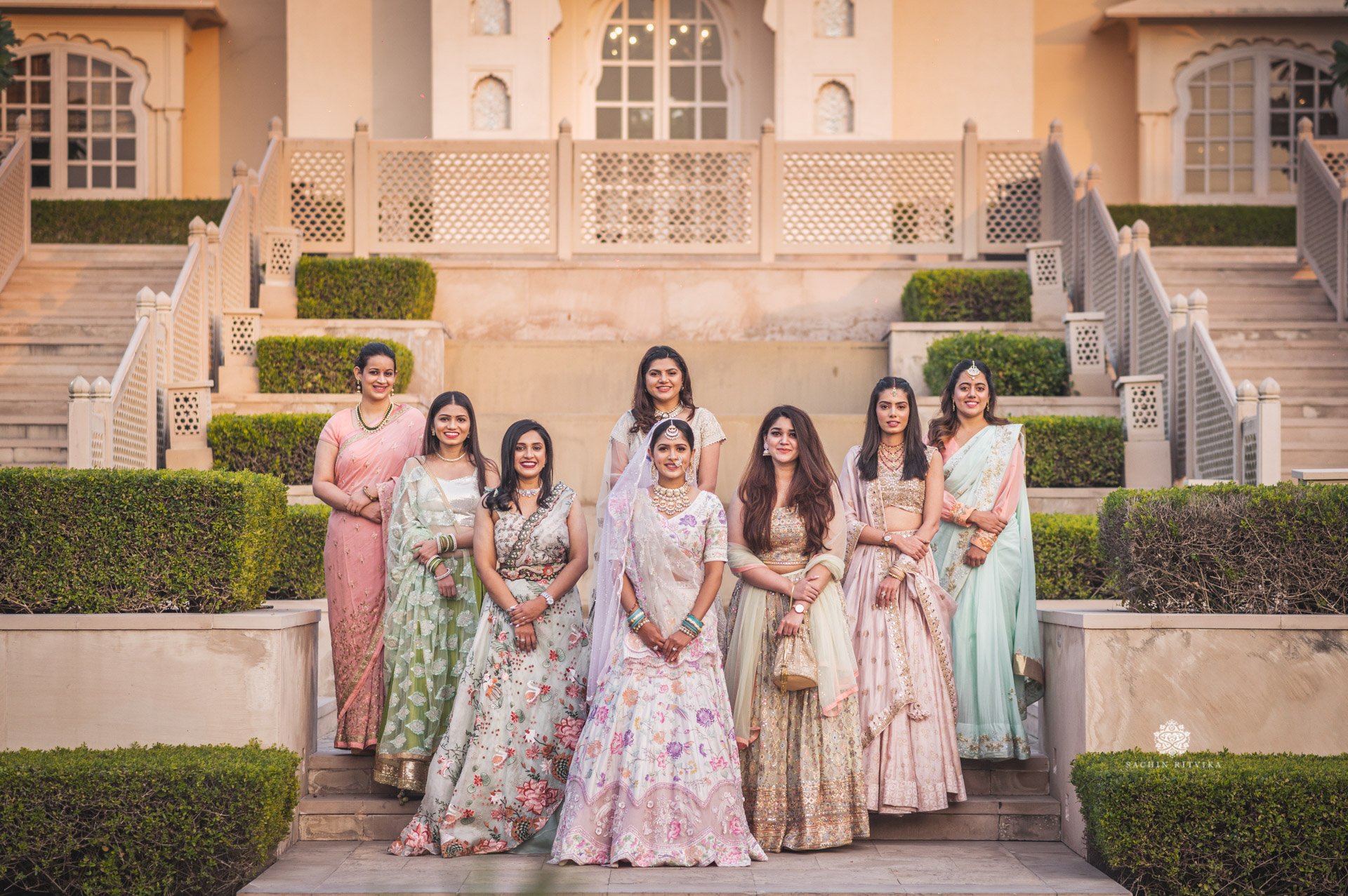 Group of women in traditional Indian attire posing in front of a building with steps and greenery at chandigarh 7 star luxury hotel.