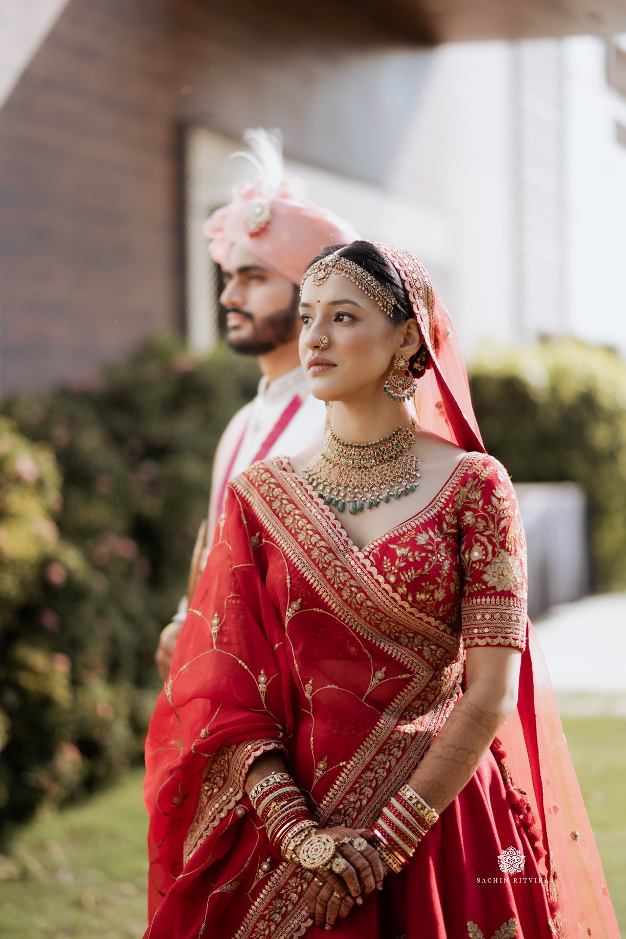Bride in red and groom in off white traditional Indian wedding attire, outdoors