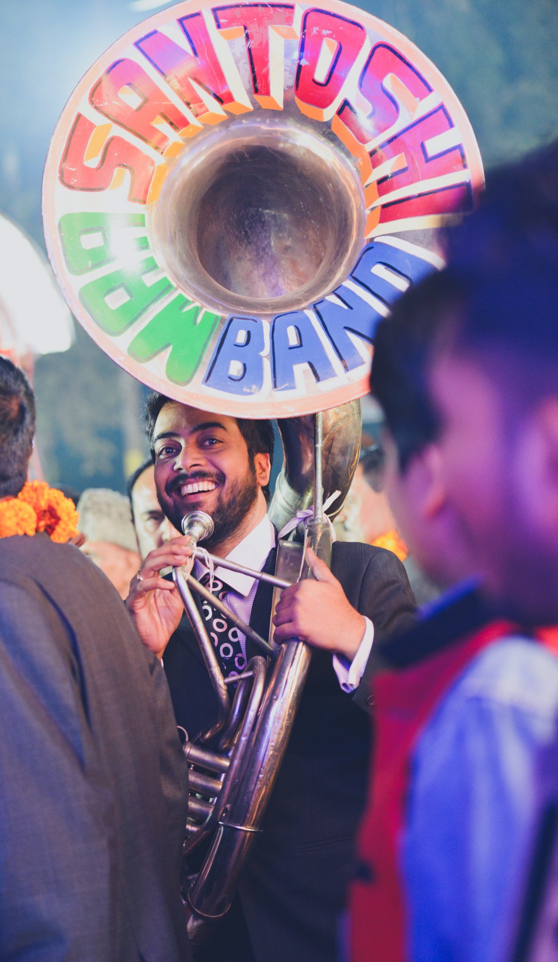 Photographers Sachin also an amateur musician playing tuba in festive band of indian baraat ceremony smiling and having fun at a family wedding in UP