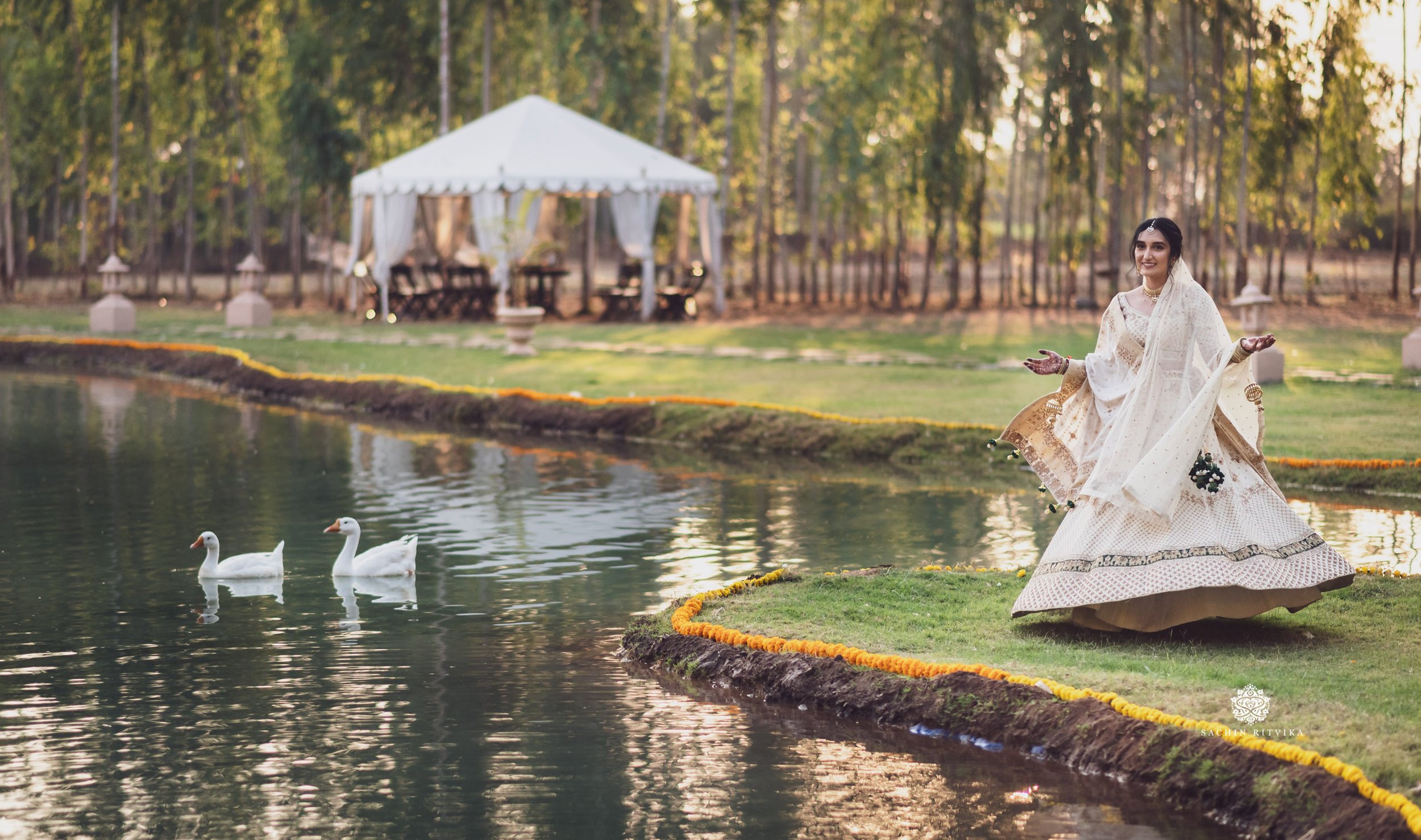 Indian Bride in traditional dress near pond with two ducks, white canopy tent in background, outdoor wedding venue at Pawagarh Resort near Vadodara India.