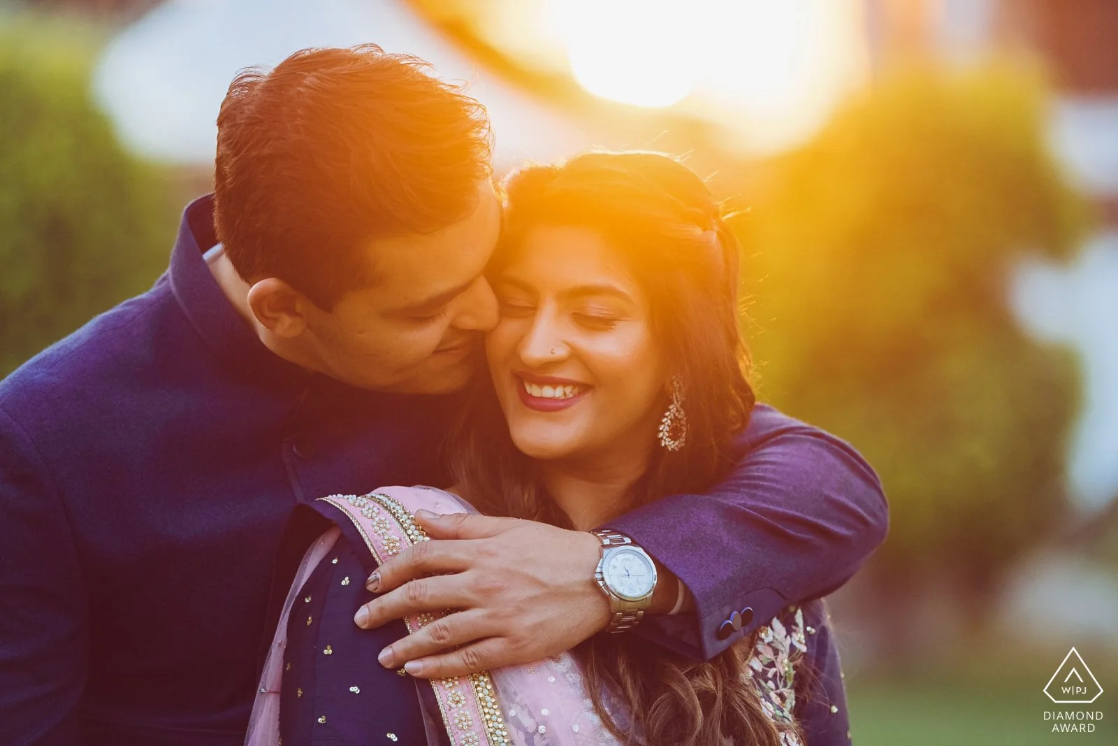 A man embracing a woman outdoors during sunset, both smiling and appearing happy.