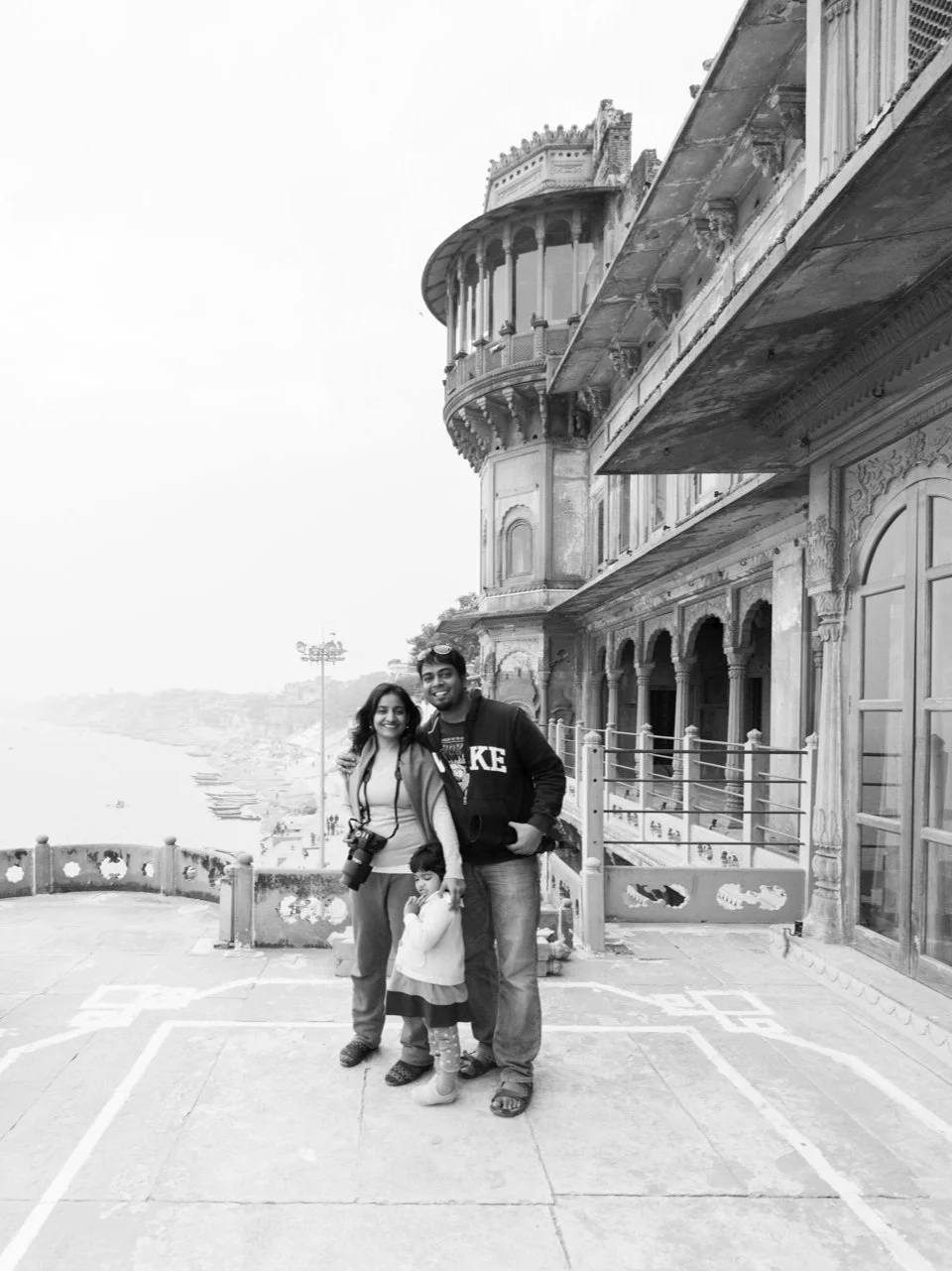 SachinRitvika photographer and travelers  posing on a rooftop terrace with ornate architecture, overlooking a body of water and distant buildings, in a black-and-white photo in benaras India