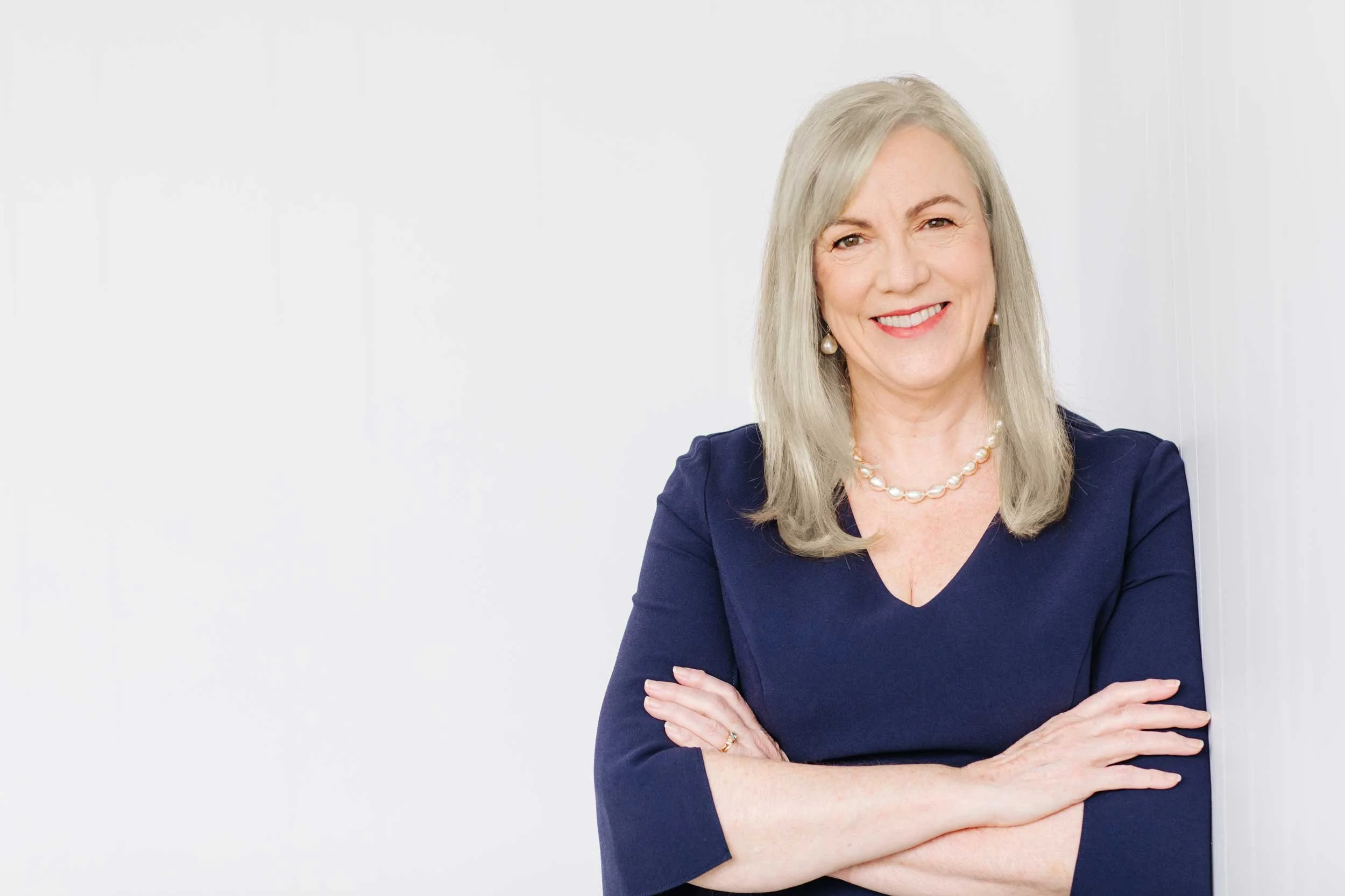 Fiona Robertson arms crossed leaning against a wall in a light indoor setting.
