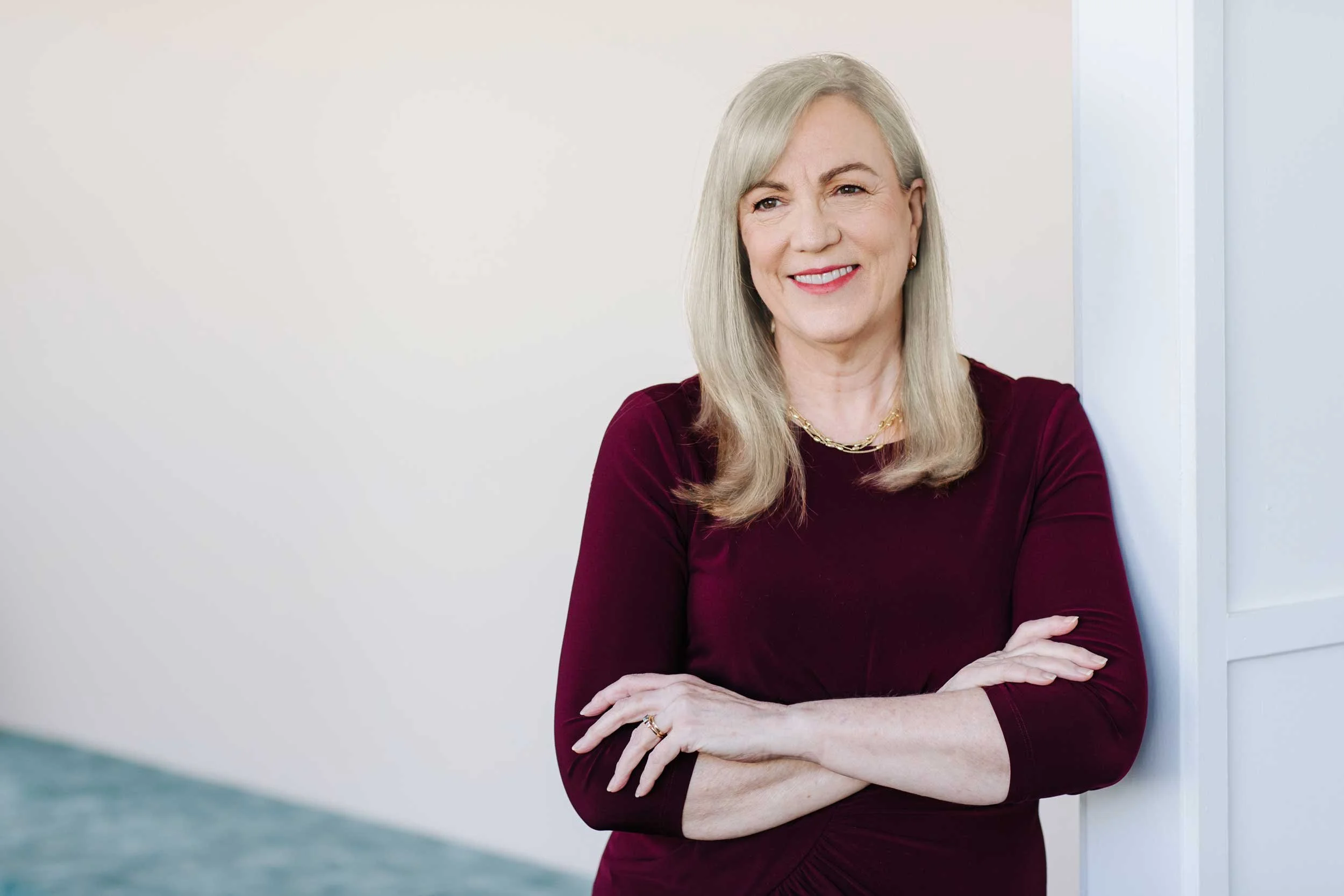Fiona Robertson standing indoors with her arms crossed, smiling against a wall.