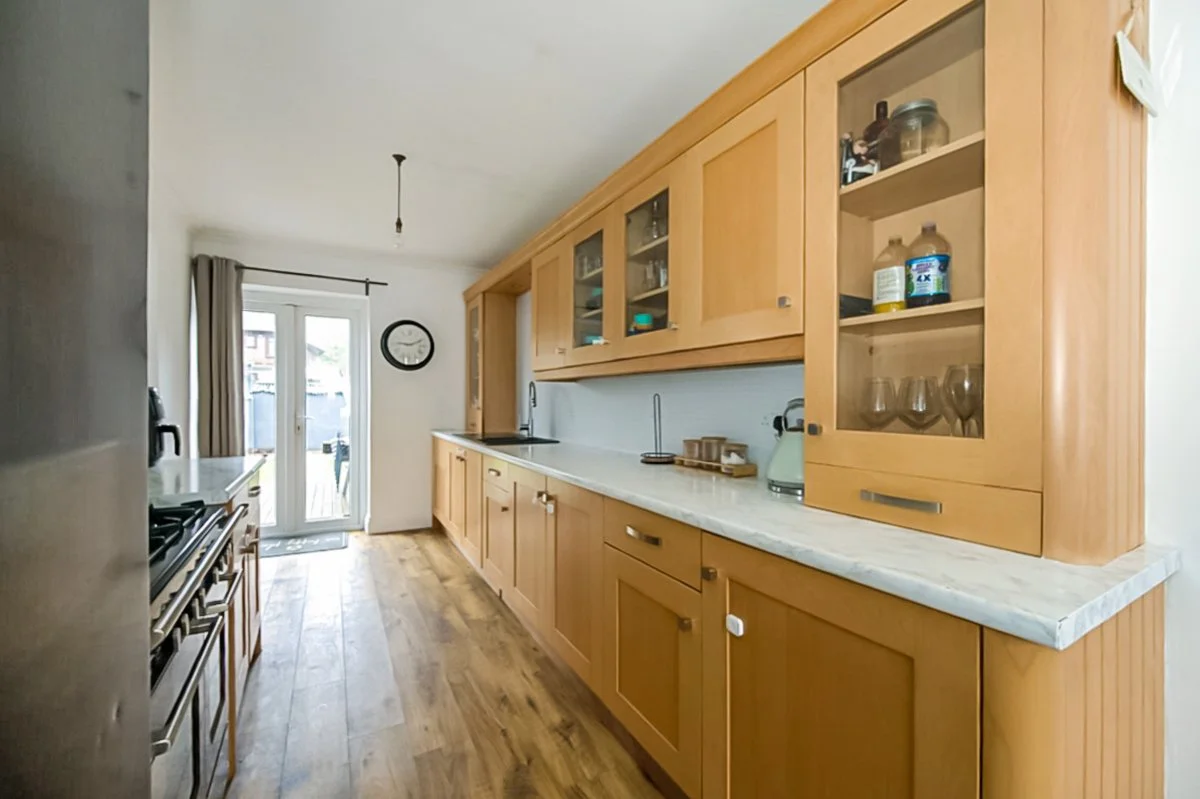 A kitchen with wooden cabinets, a marble countertop, and a door leading outside. There is a clock on the wall and a chandelier hanging from the ceiling.