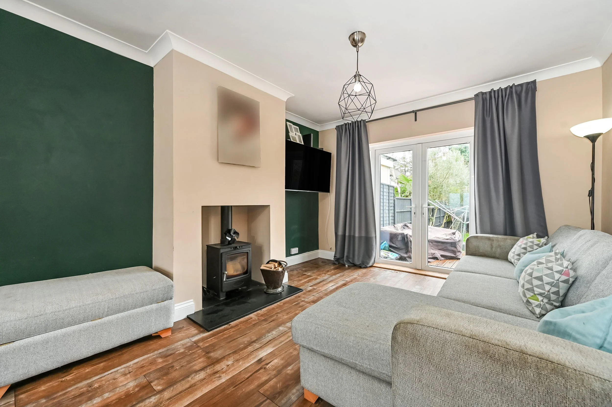 Living room with grey sofa, green accent wall, fireplace, television, dark curtains, and glass door leading to outdoor patio.