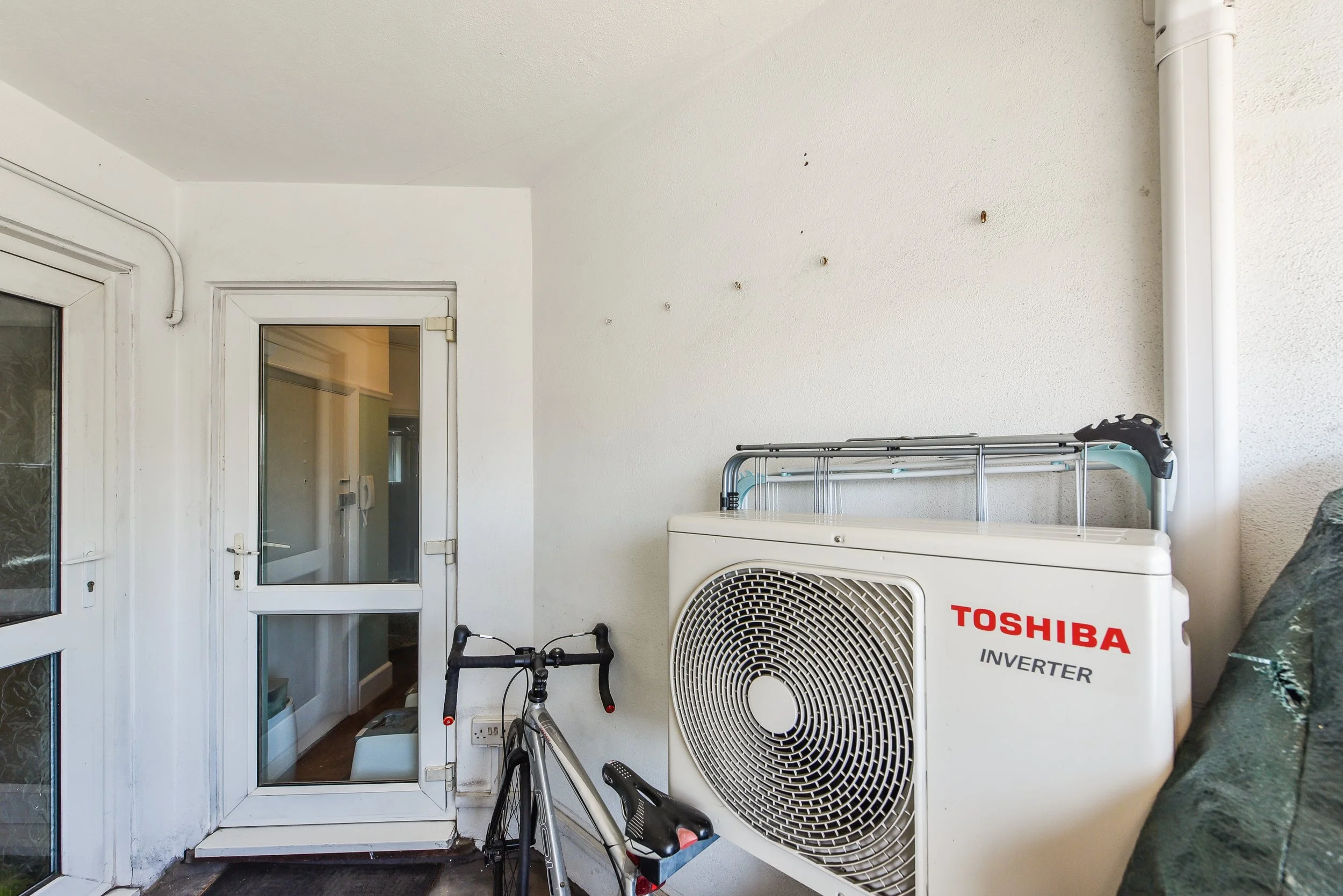 Balcony with white Toshiba inverter air conditioning unit, black bicycle, and a door leading to an interior room.