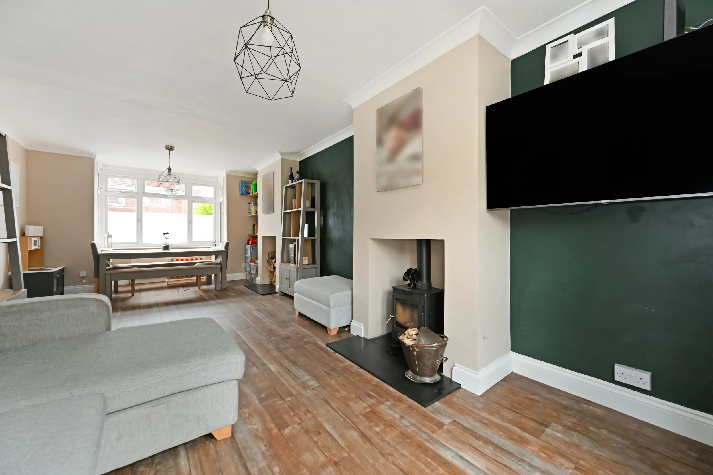Living room with light gray sofa, dark green accent wall, fireplace, TV mounted on wall, wooden floor, and windows letting in natural light.