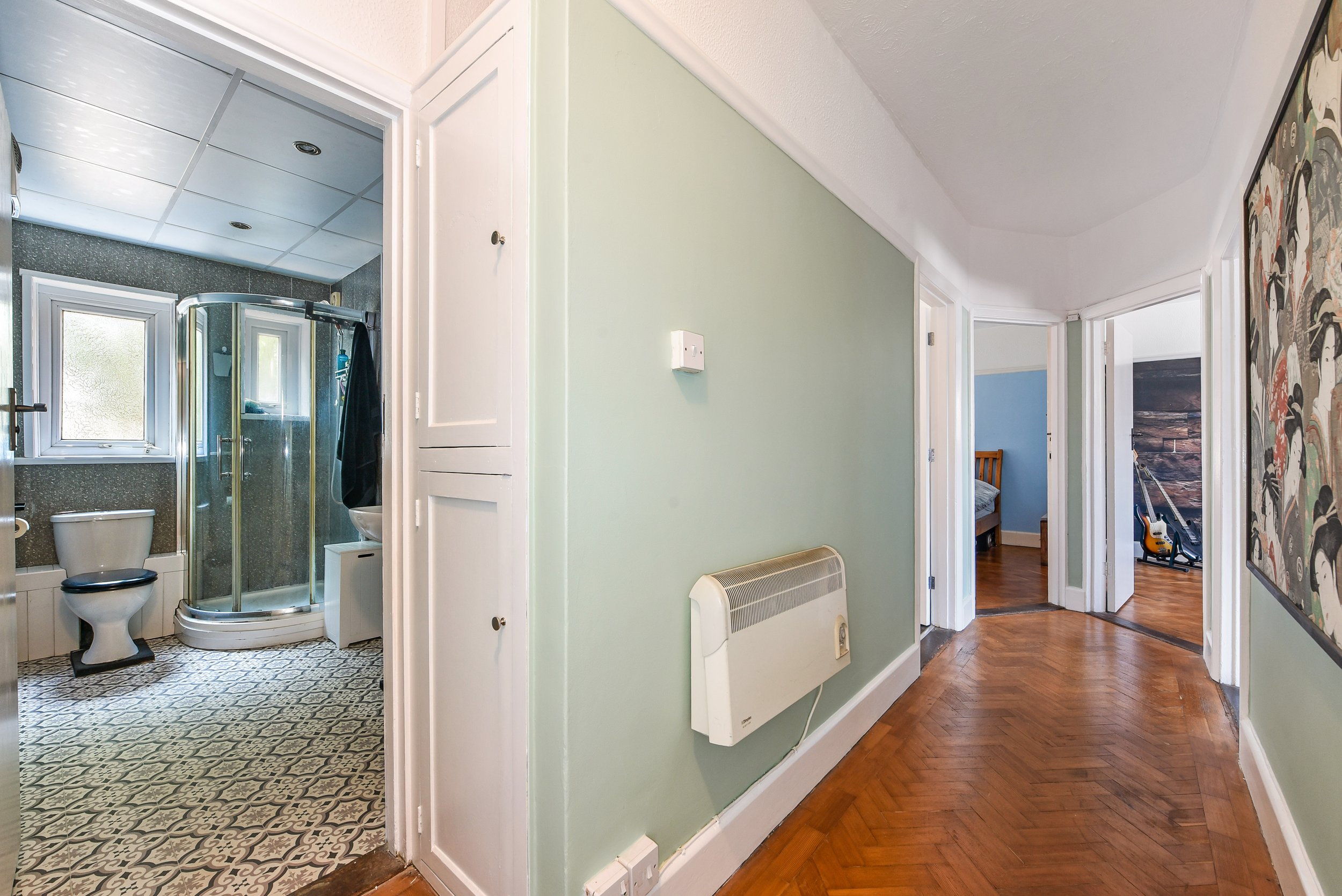 Hallway with green walls leading to bedrooms and a bathroom, with a hardwood floor, heater on the wall, and a piece of framed art on the right wall.