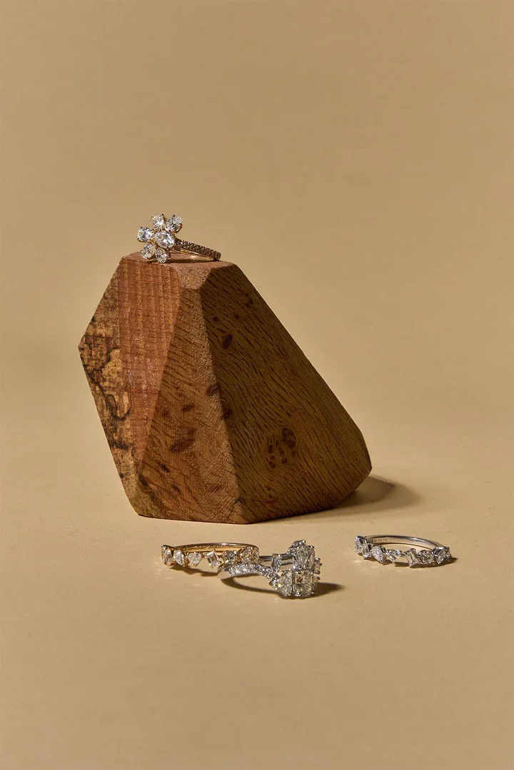 A wooden block displaying a diamond ring on top and three diamond rings placed at its base.
