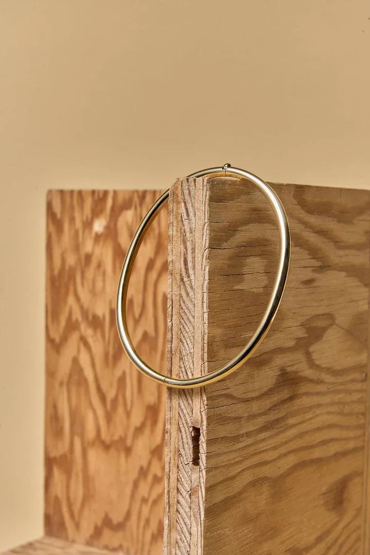 A close-up of a simple gold or brass ring hanging on a piece of unfinished wooden furniture, possibly a door or a cabinet, with a beige wall in the background.