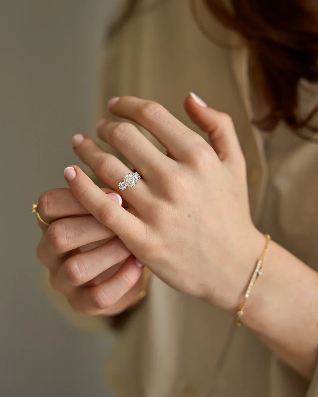 Close-up of a woman’s hands showing a sparkling diamond engagement ring on her ring finger, with additional gold jewelry on her wrists.